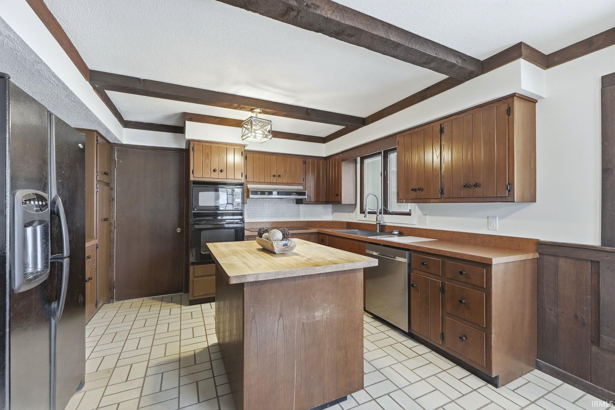 Kitchen with brick patterned flooring, black appliances, a center island, wood counters, and beamed ceiling