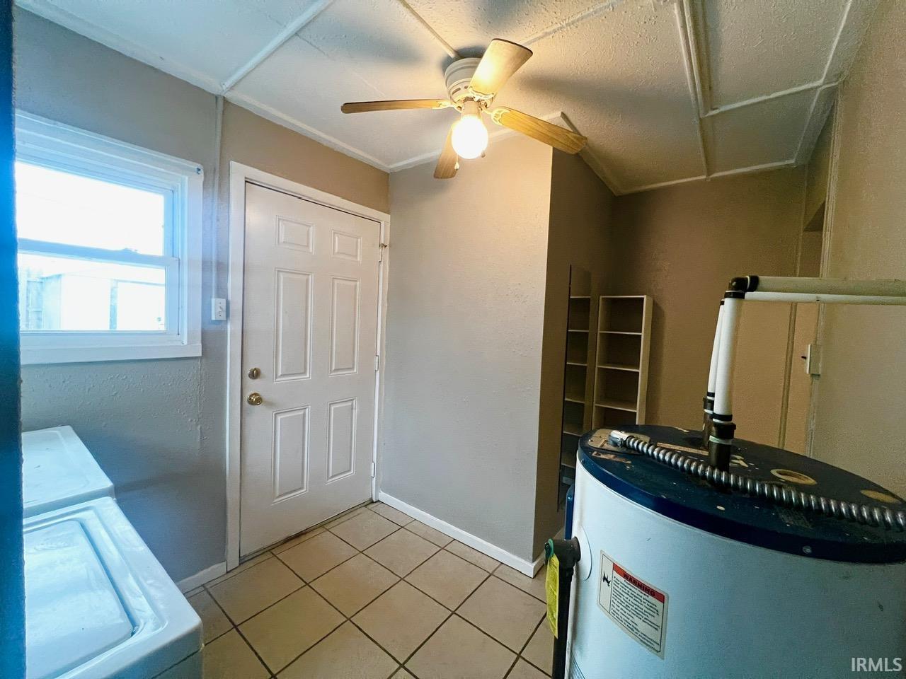 Foyer featuring water heater, washer / dryer, light tile patterned floors, and a ceiling fan