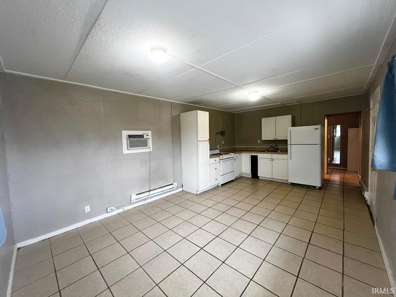 Kitchen featuring white cabinets, white appliances, baseboard heating, light countertops, and light tile patterned floors