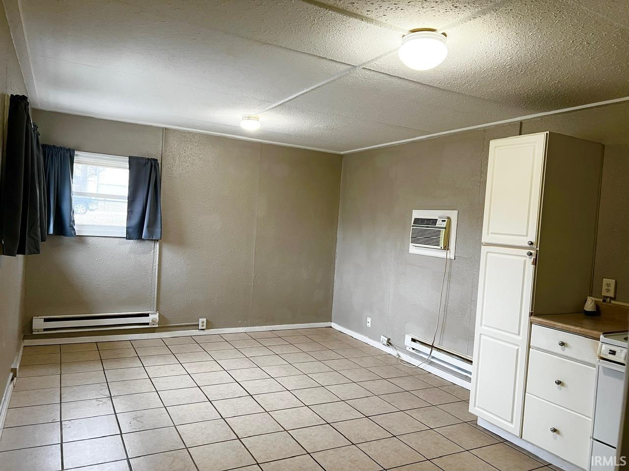 Empty room featuring a textured wall, baseboard heating, a baseboard heating unit, an AC wall unit, and light tile patterned floors