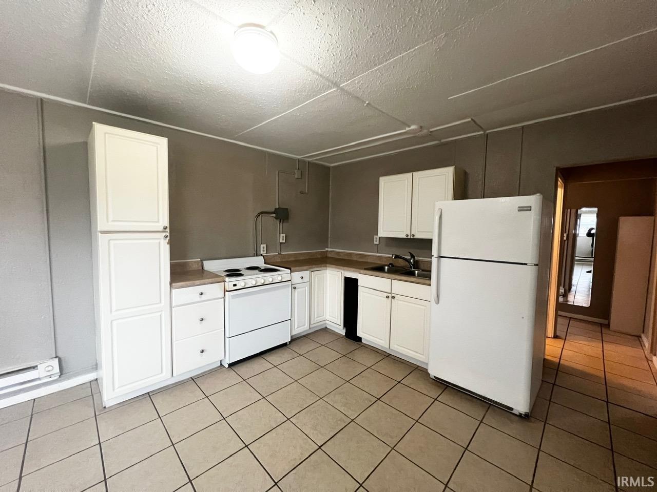 Kitchen featuring white cabinets, white appliances, light countertops, and a textured ceiling