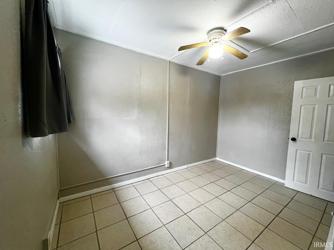 Empty room featuring a textured wall, a ceiling fan, and light tile patterned floors