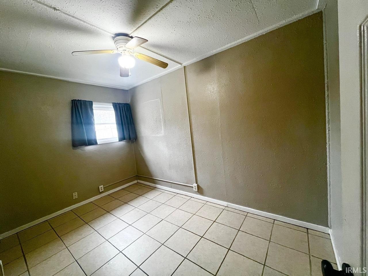 Unfurnished room featuring a textured wall, light tile patterned floors, and ceiling fan