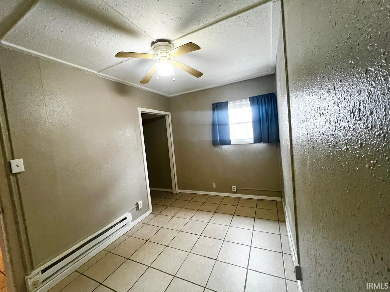 Spare room with a baseboard radiator, a textured wall, light tile patterned floors, and a ceiling fan