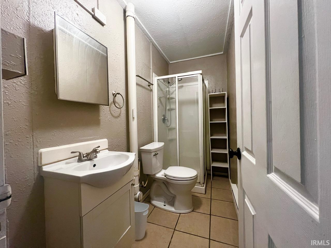 Bathroom featuring a textured wall, vanity, a stall shower, light tile patterned flooring, and a textured ceiling