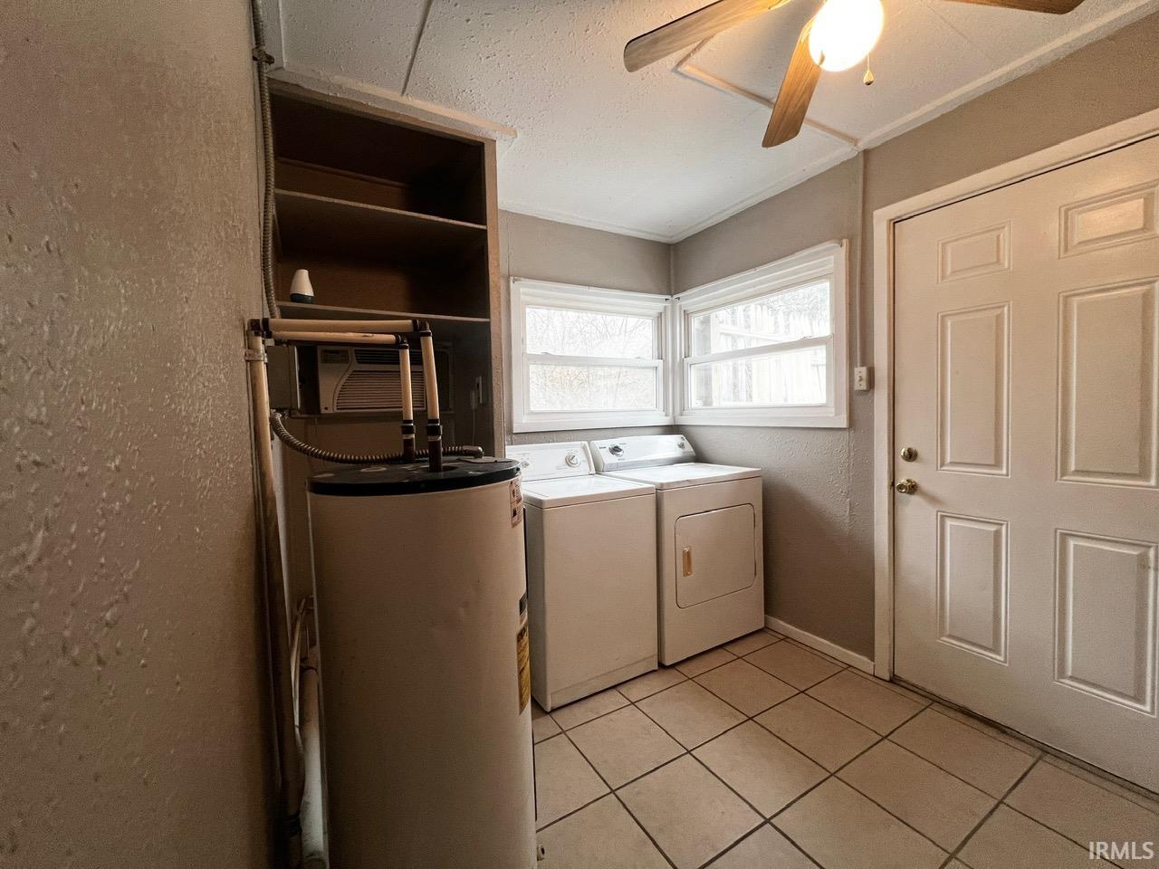 Washroom featuring water heater, washer and dryer, a textured wall, light tile patterned floors, and a ceiling fan