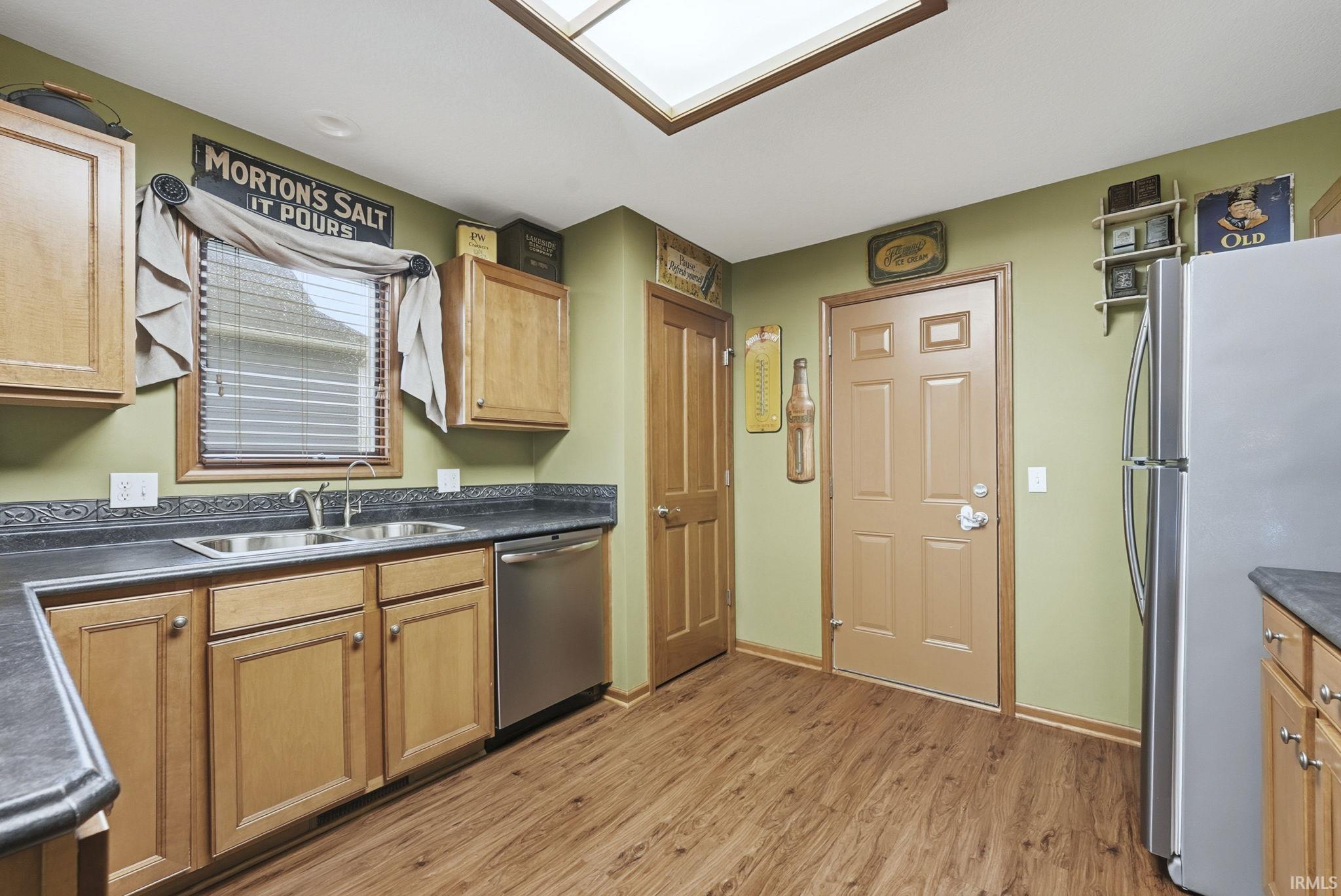Kitchen featuring dark countertops, stainless steel appliances, light wood finished floors, a skylight, and brown cabinets