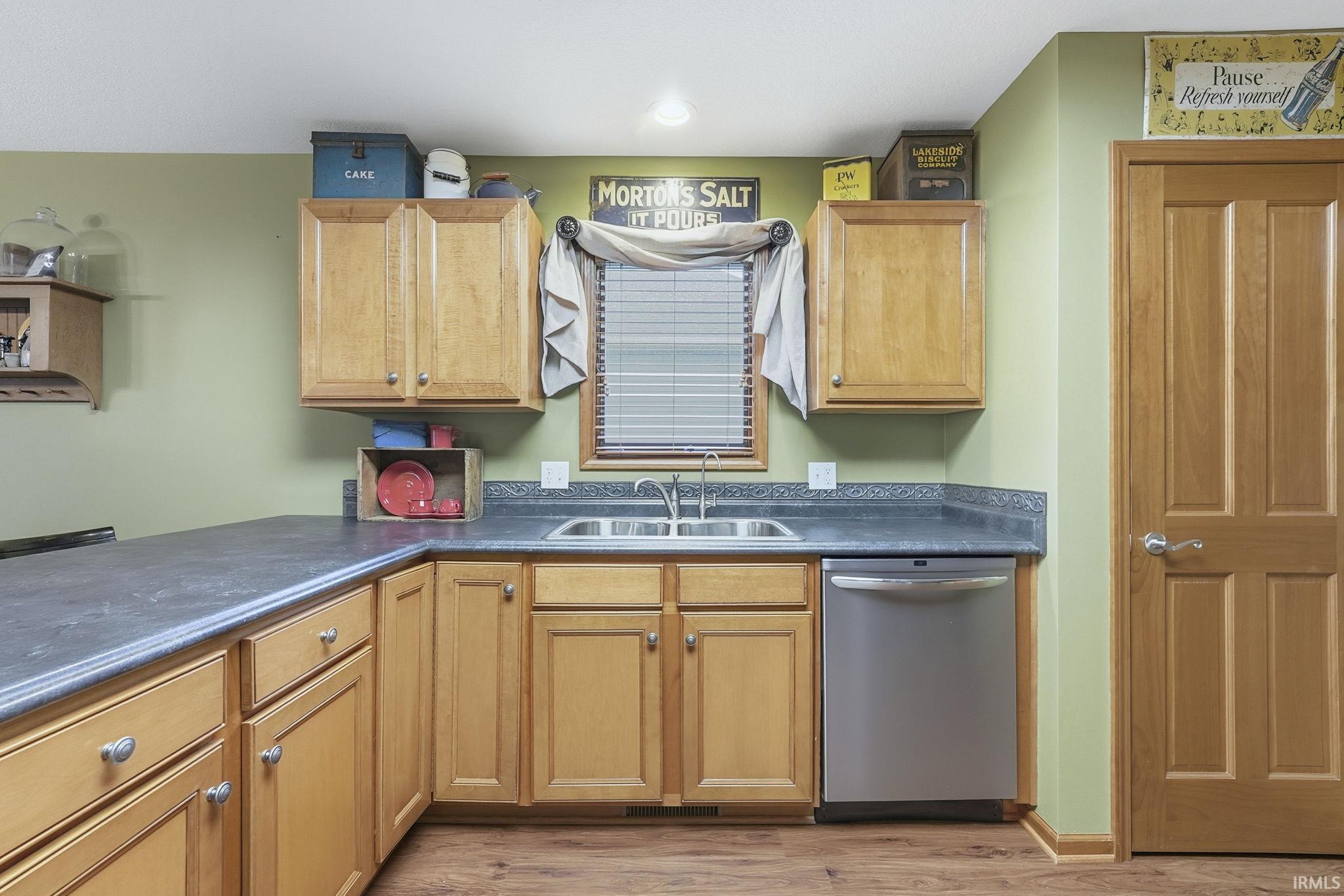 Kitchen with stainless steel dishwasher, dark countertops, and light wood-style floors