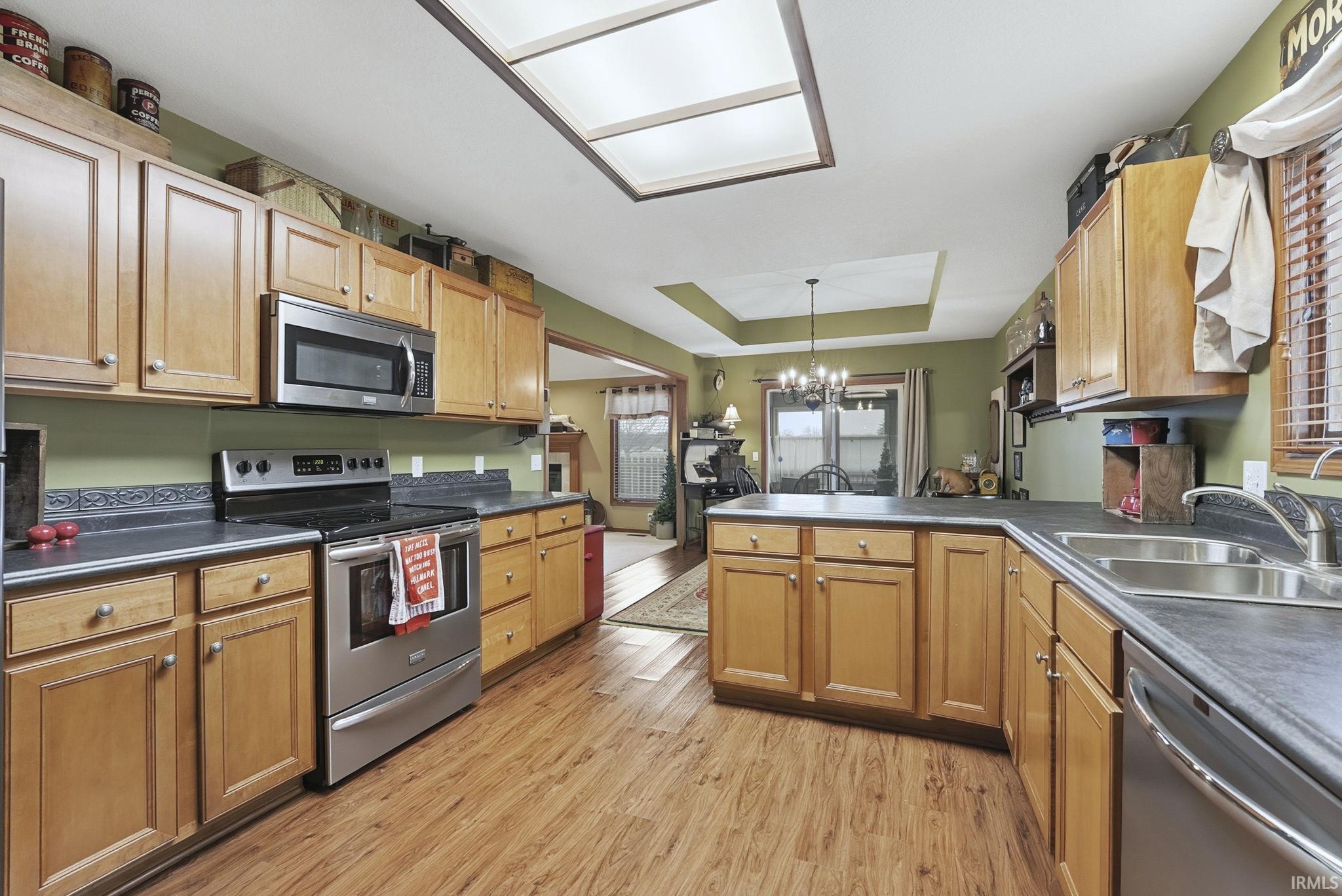 Kitchen with a tray ceiling, stainless steel appliances, decorative light fixtures, a chandelier, and a peninsula