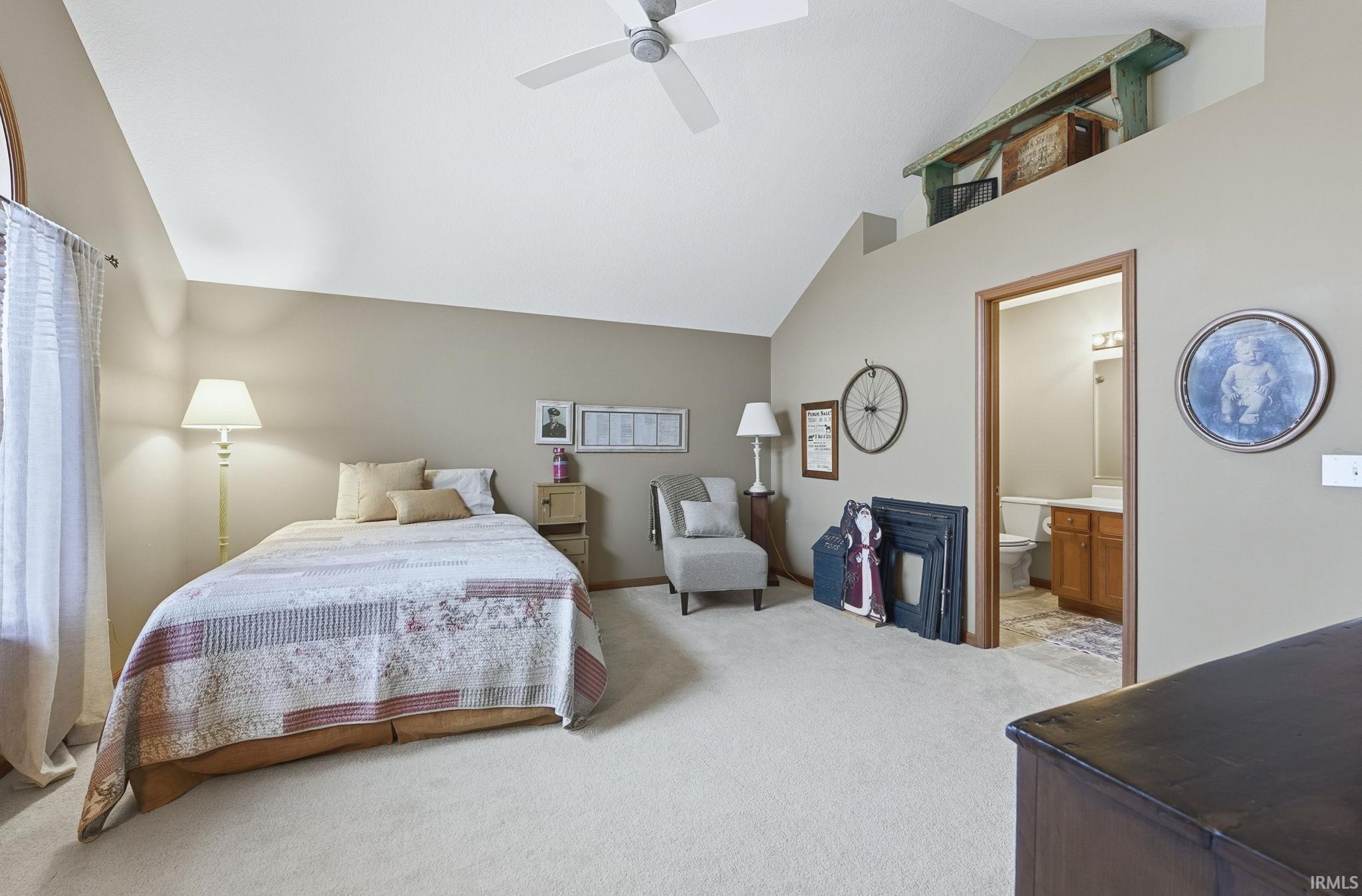 Bedroom featuring light colored carpet, ceiling fan, high vaulted ceiling, and connected bathroom