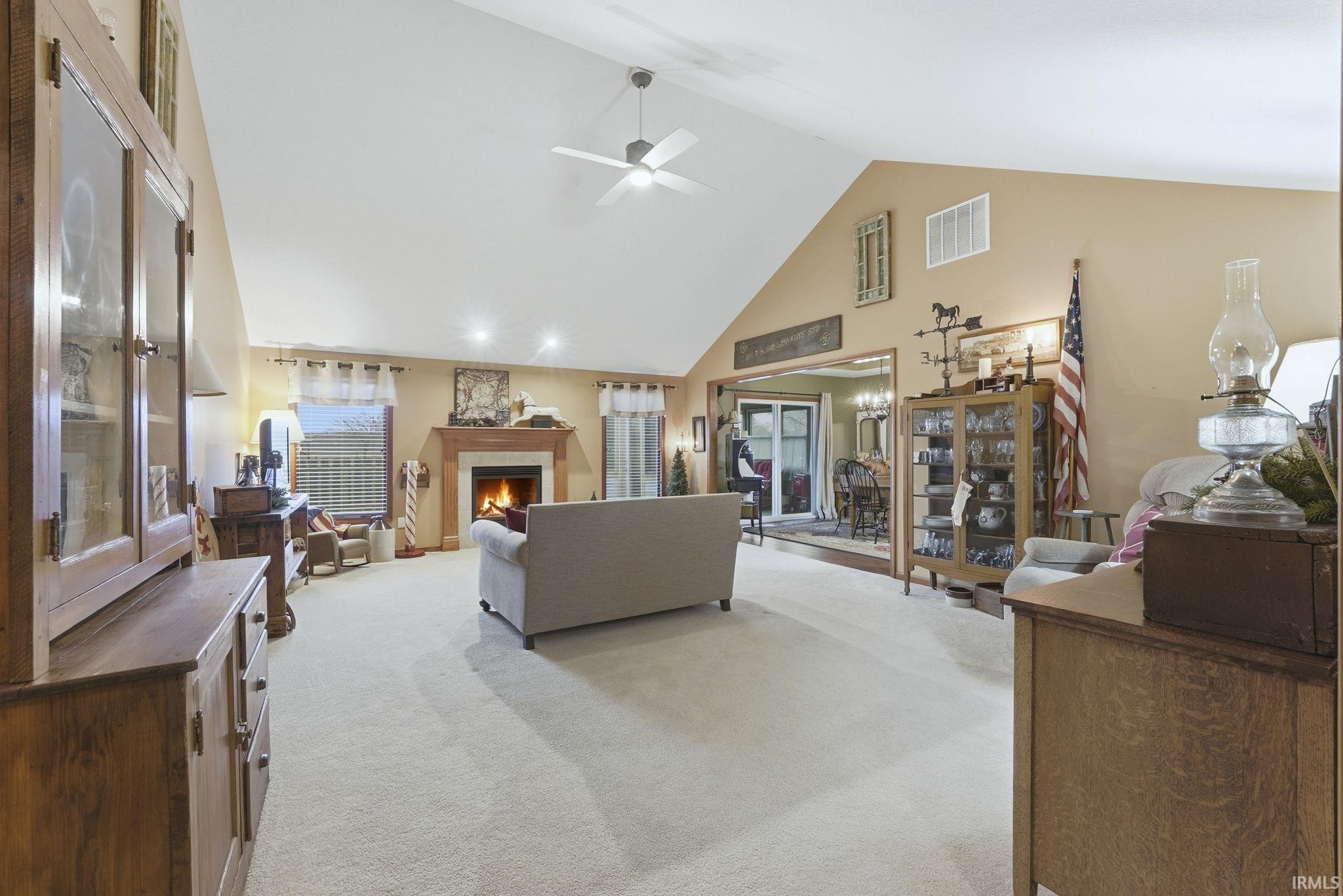 Living area with high vaulted ceiling, light colored carpet, a lit fireplace, and ceiling fan