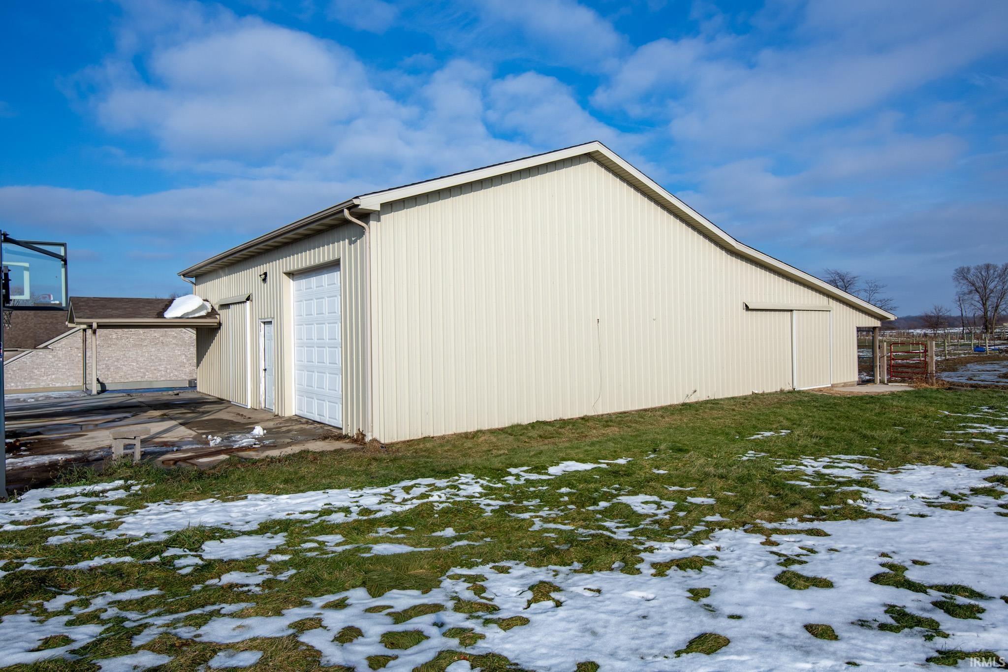 View of snowy exterior with an outdoor structure, a detached garage, and a pole building