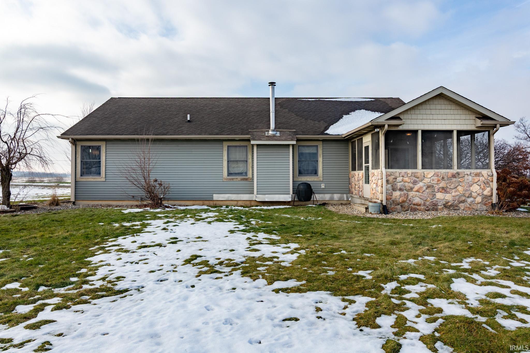 Snow covered back of property with a sunroom, a shingled roof, a yard, and stone siding
