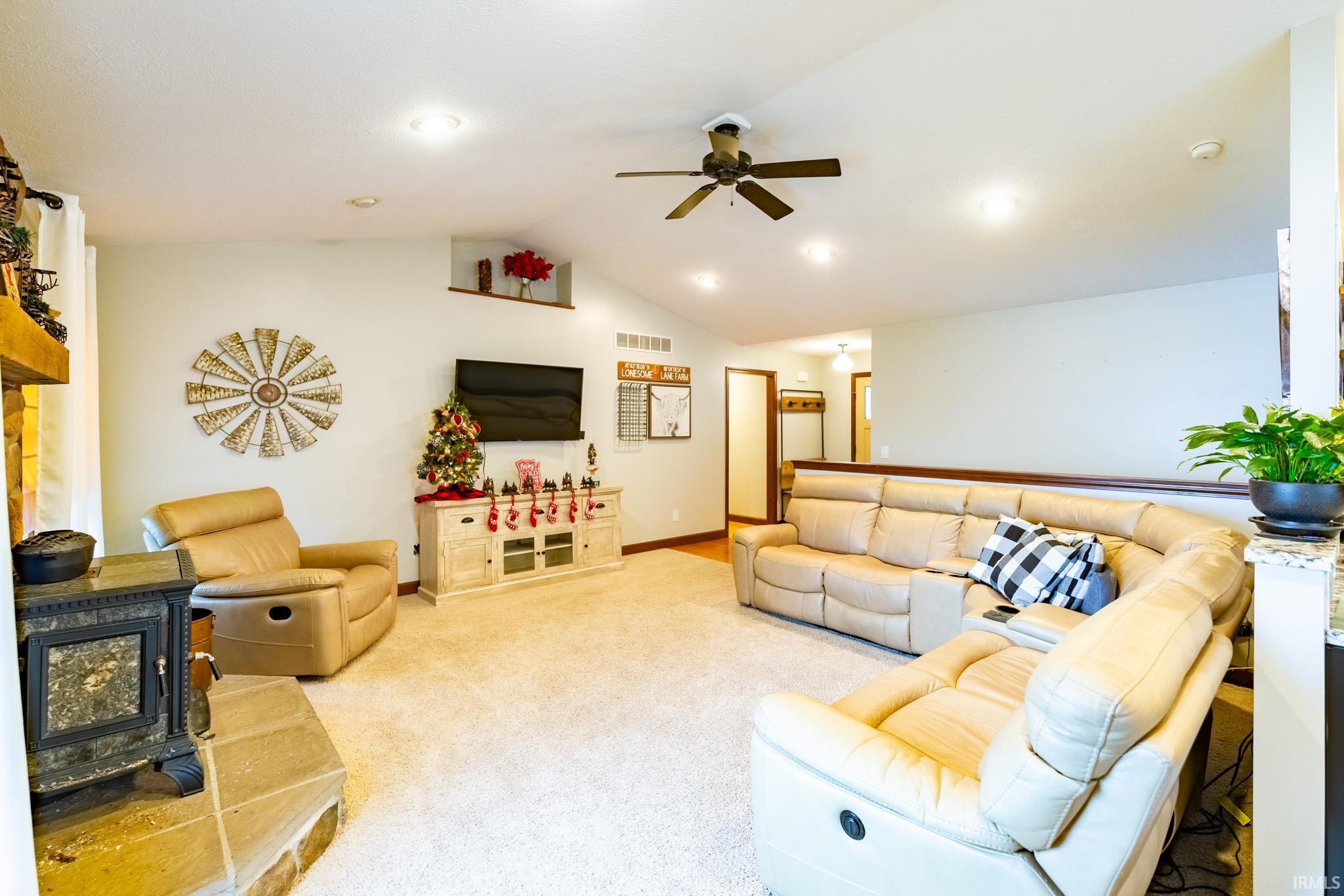 Living area featuring a wood stove, vaulted ceiling, carpet flooring, recessed lighting, and a ceiling fan