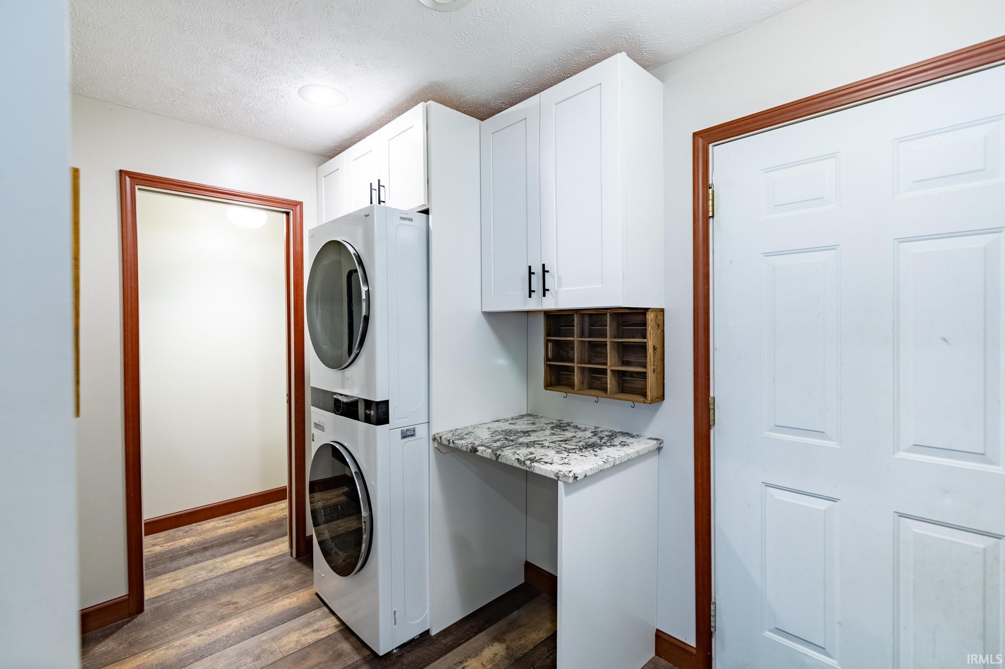 Laundry room with dark wood-style floors, stacked washing machine and dryer, and a textured ceiling
