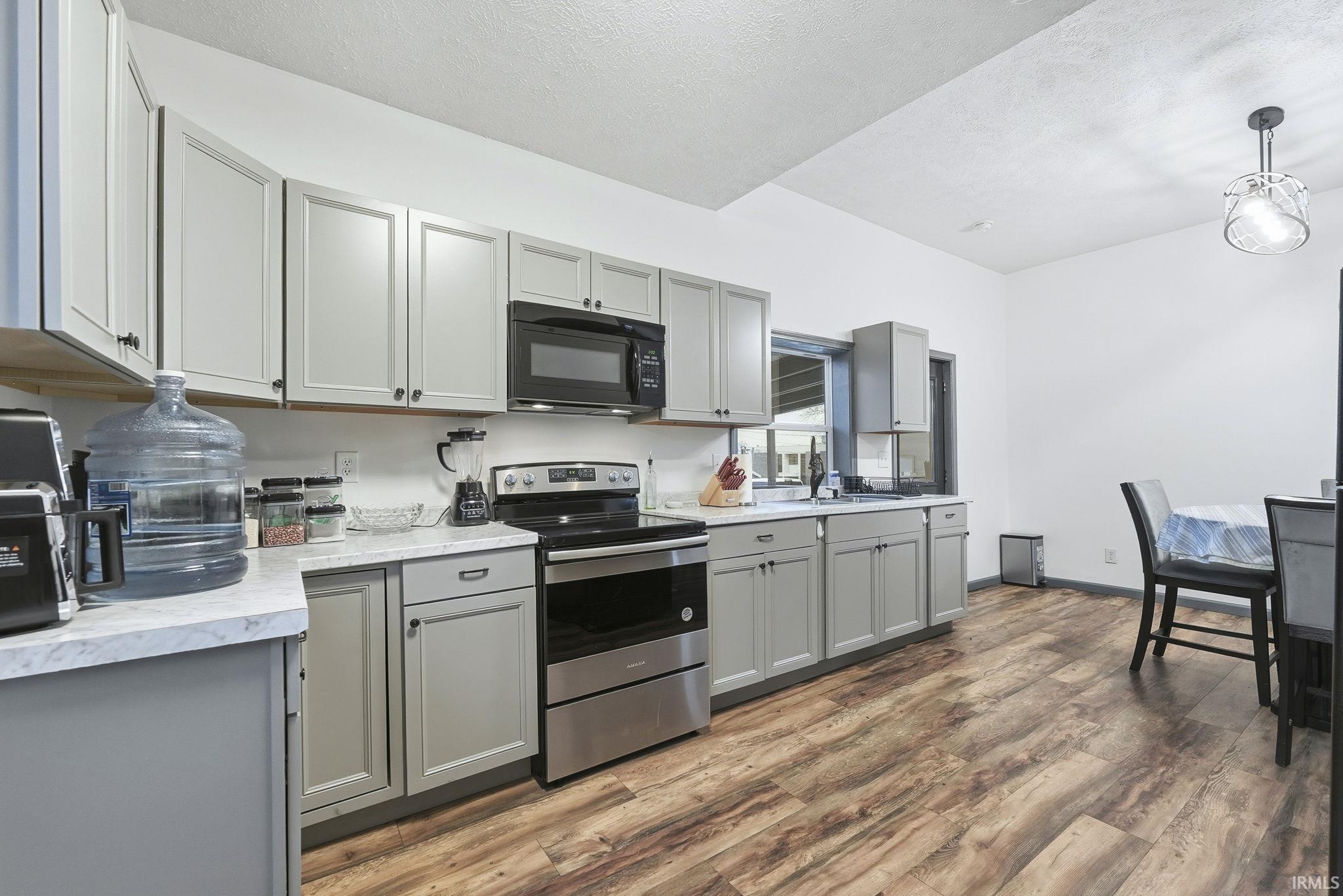 Kitchen featuring gray cabinets, electric range, light countertops, black microwave, and dark wood-type flooring