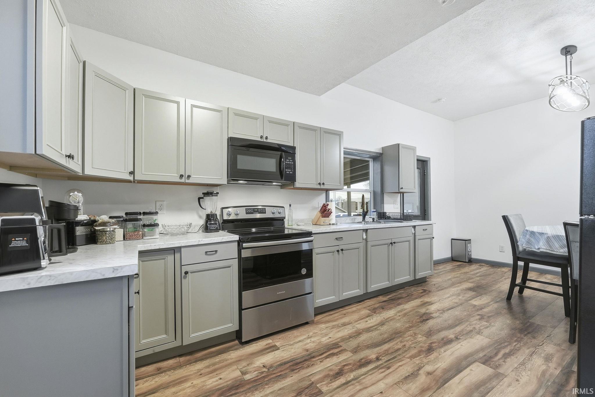 Kitchen with gray cabinetry, stainless steel electric range, light countertops, black microwave, and light wood finished floors