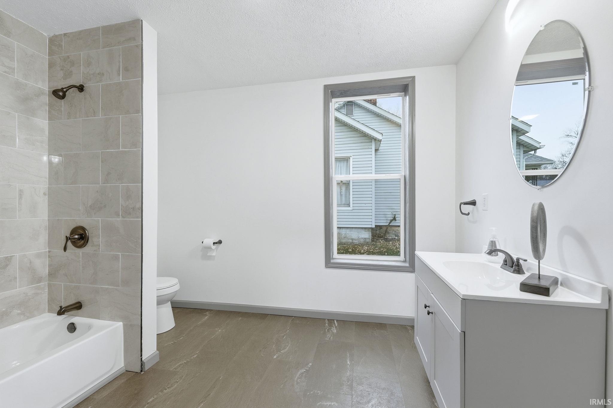 Bathroom with vanity, washtub / shower combination, a textured ceiling, and light wood-style floors