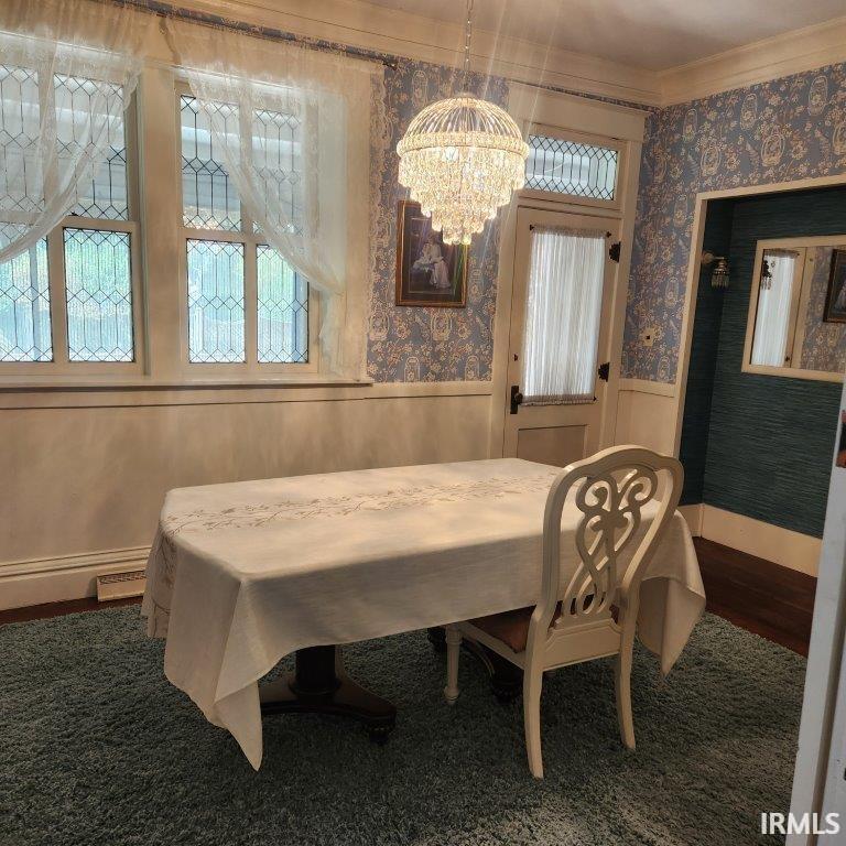 Dining room with wallpapered walls, wainscoting, a chandelier, baseboard heating, and ornamental molding