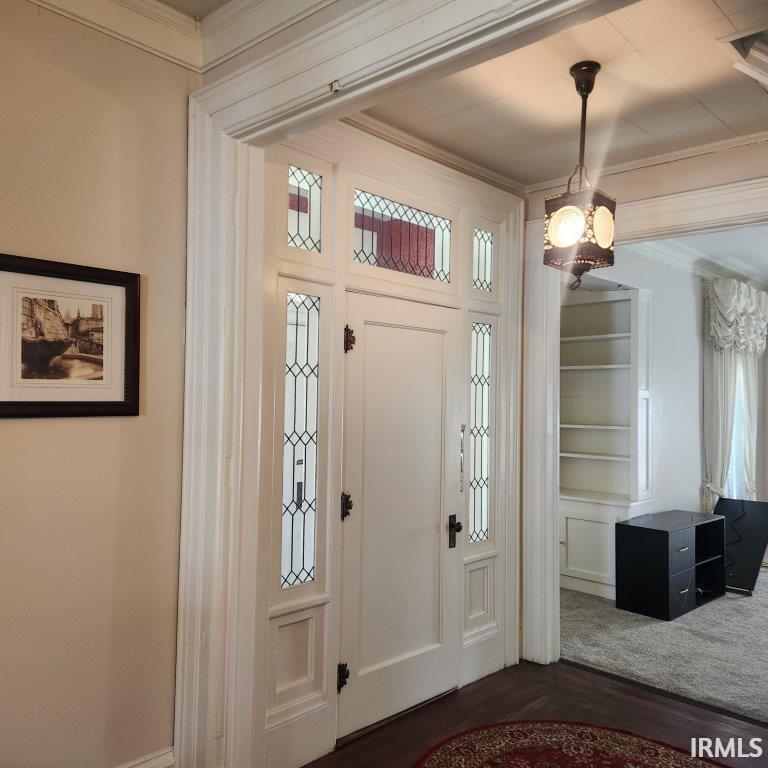 Foyer with crown molding, dark wood-type flooring, and a chandelier