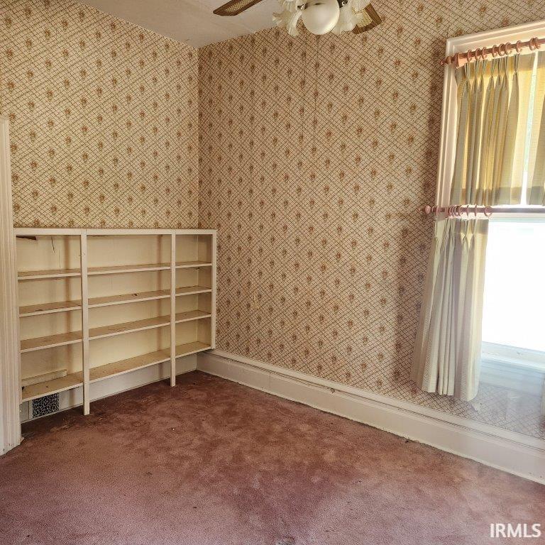 Additional living space with dark carpet, wallpapered walls, and a ceiling fan