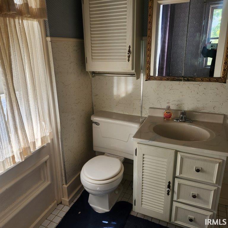 Half bath featuring vanity, wallpapered walls, and light tile patterned flooring
