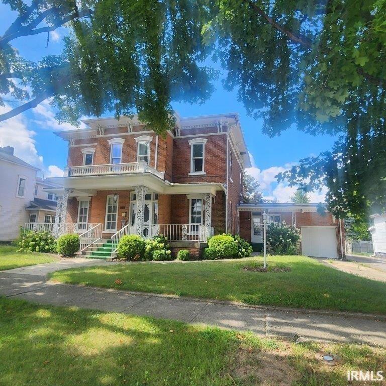 Italianate house with brick siding, covered porch, a front lawn, and a garage
