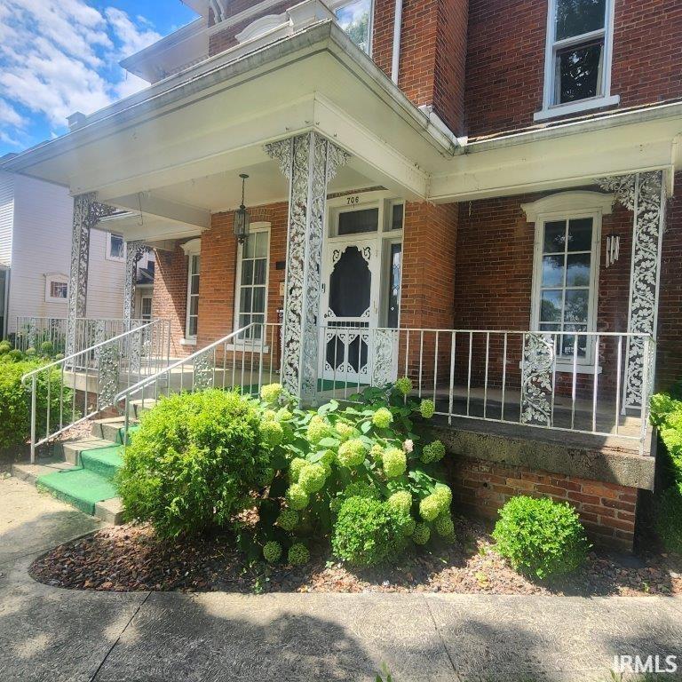 View of exterior entry featuring brick siding and a porch