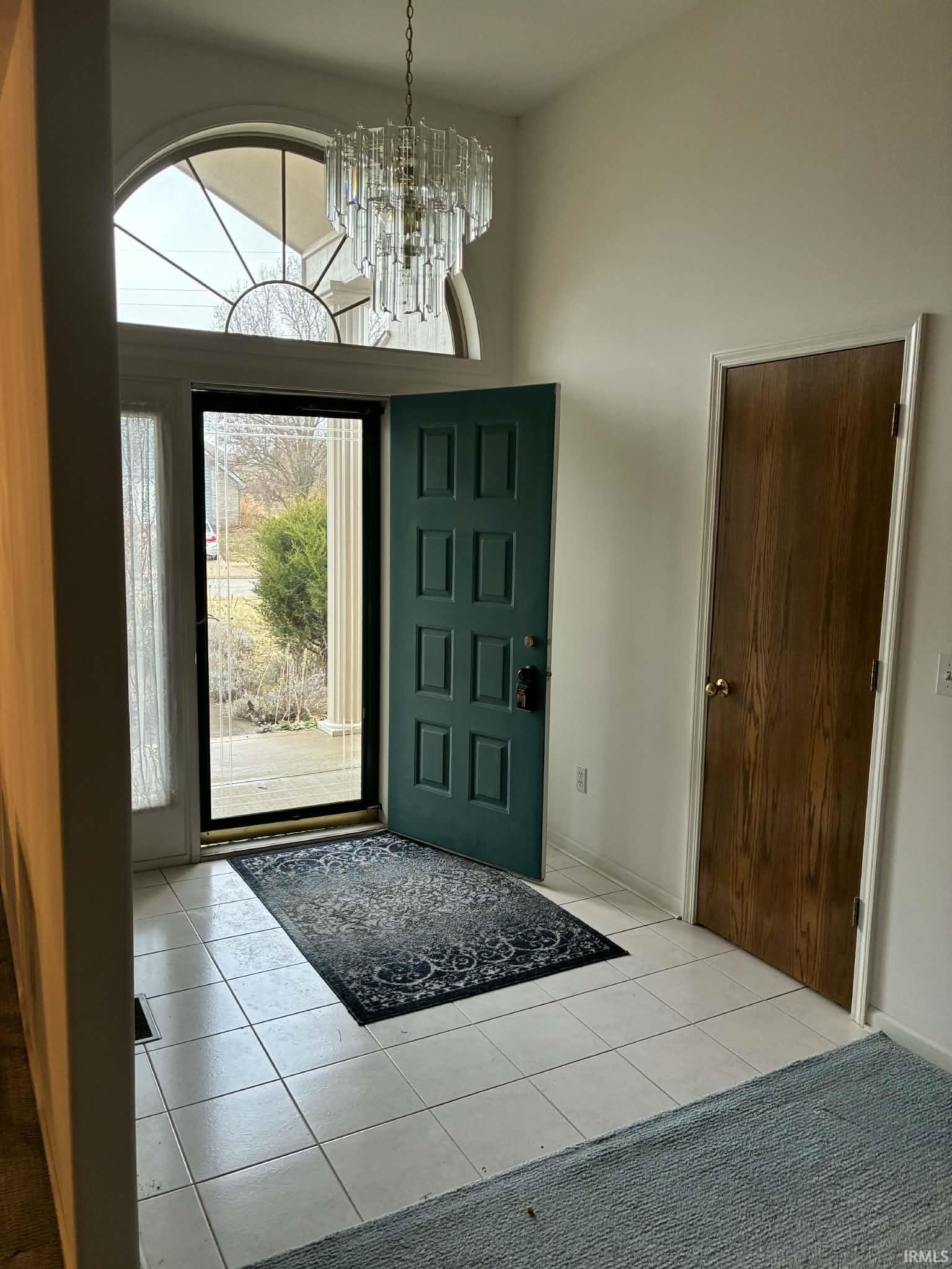 Foyer entrance with healthy amount of natural light, light tile patterned floors, a towering ceiling, and a chandelier