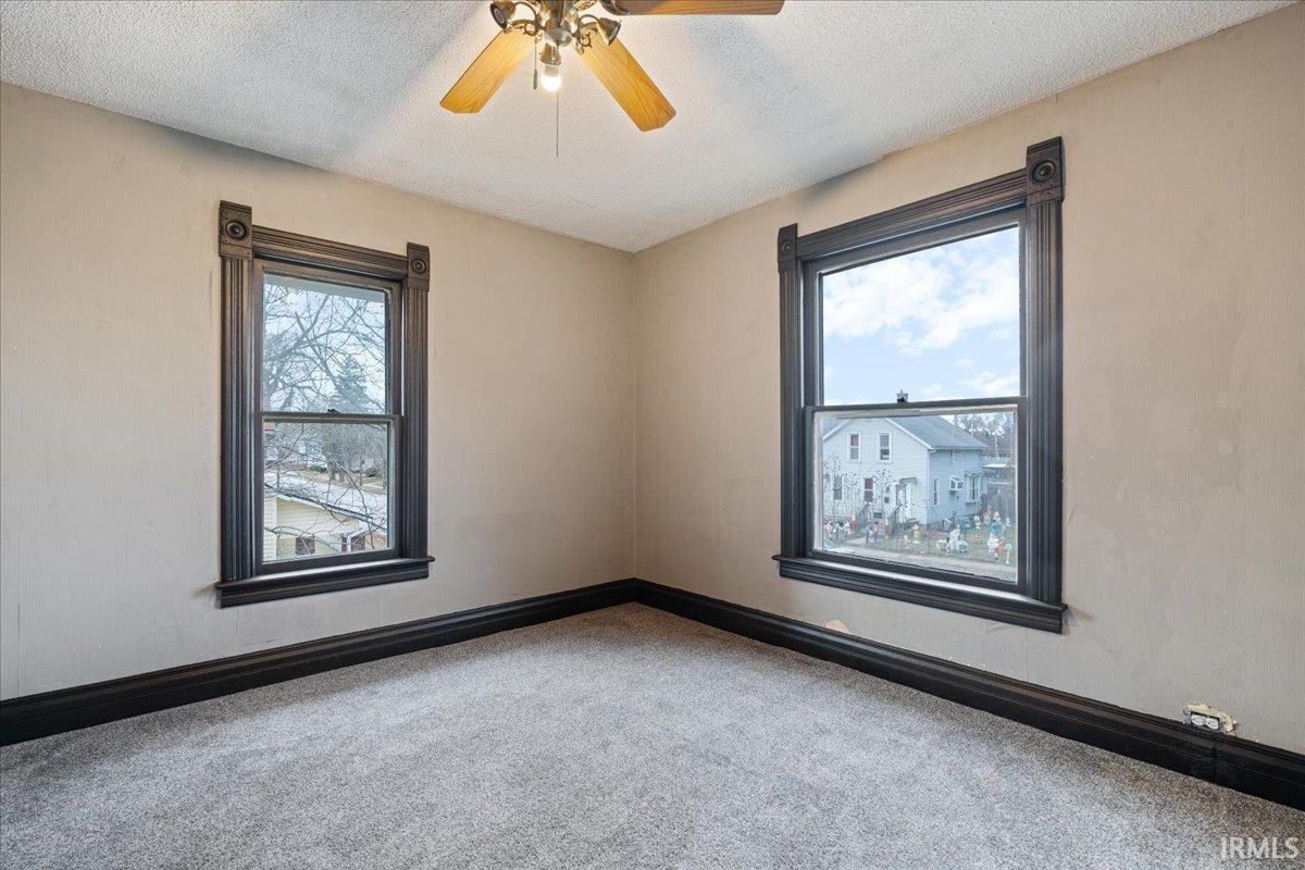 Carpeted empty room featuring a textured ceiling, a ceiling fan, and plenty of natural light