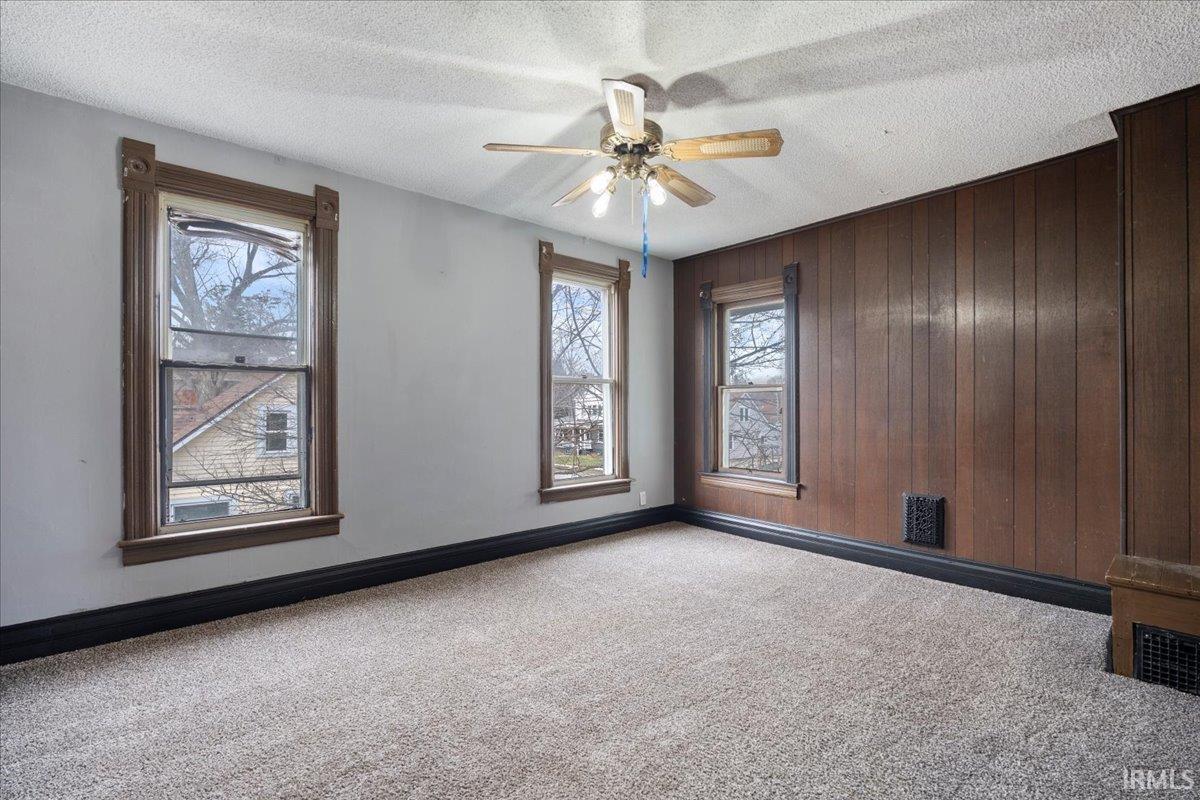 Carpeted empty room featuring a textured ceiling, wood walls, and ceiling fan