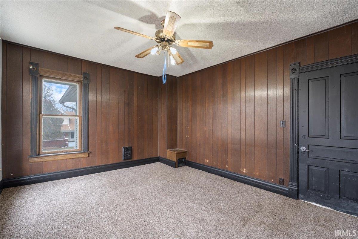 Empty room with light colored carpet, wooden walls, a textured ceiling, and ceiling fan