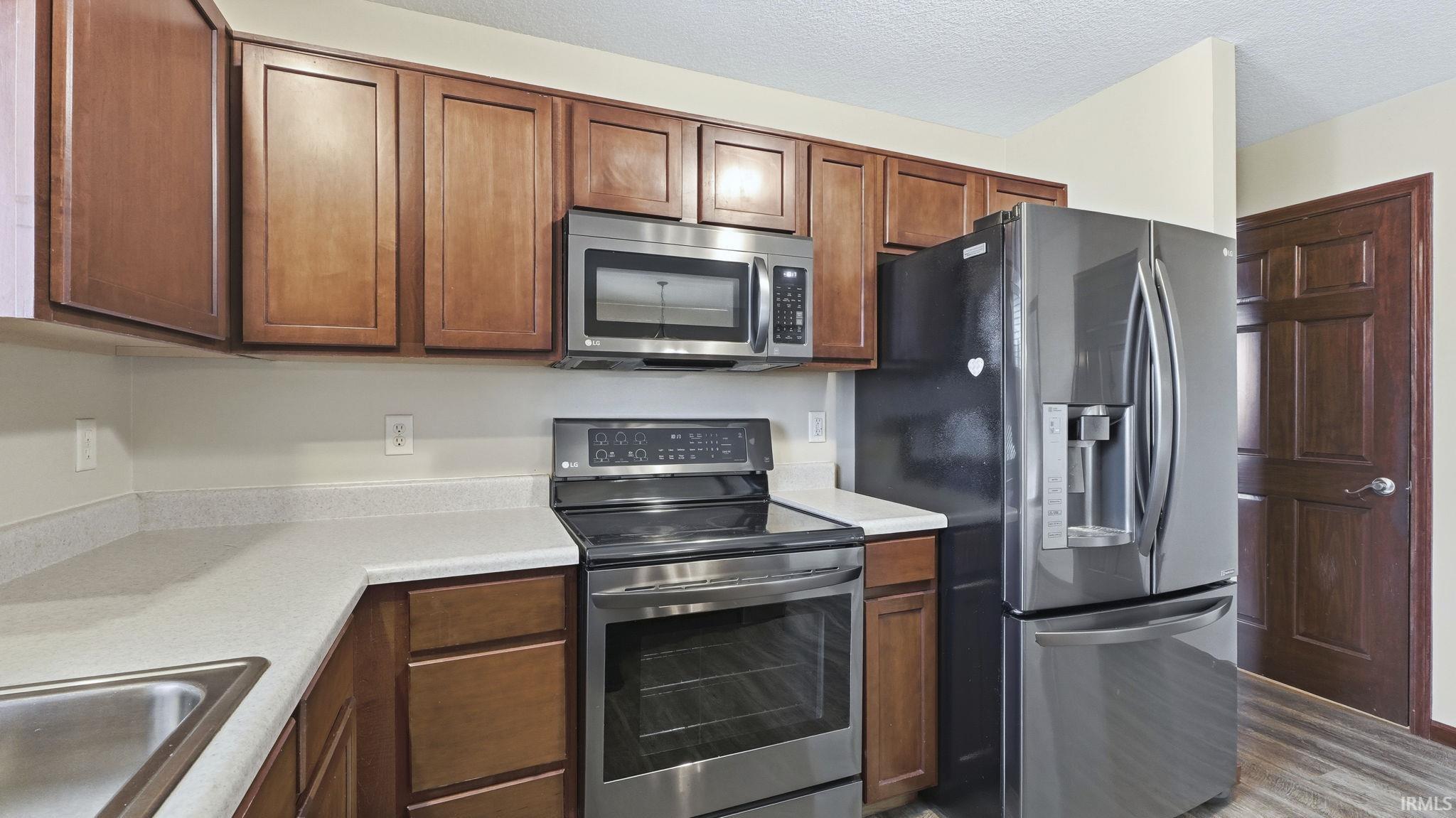 Kitchen featuring stainless steel appliances, light countertops, wood finished floors, brown cabinetry, and a textured ceiling