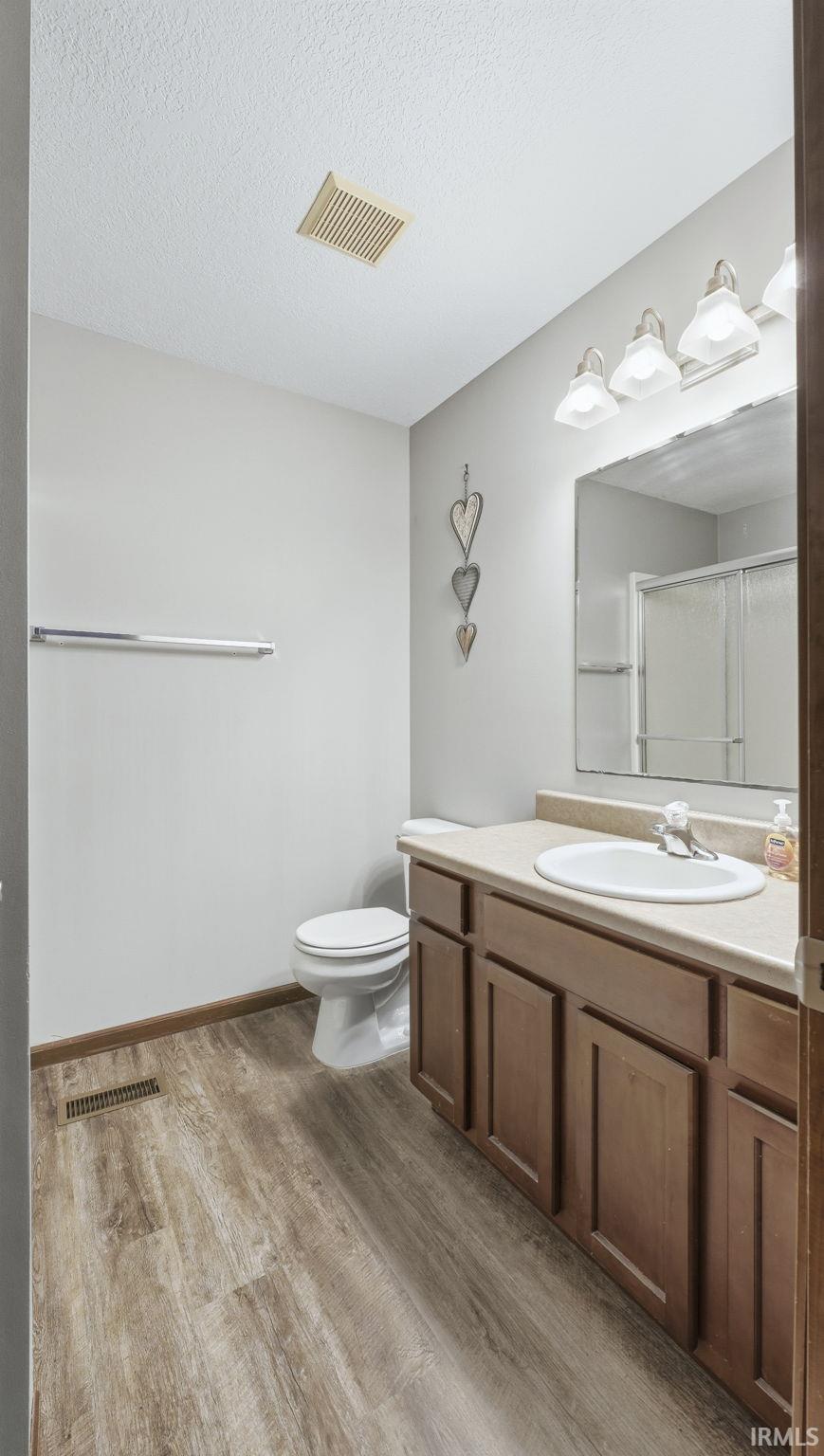 Full bathroom featuring vanity, light wood finished floors, a shower stall, and a textured ceiling
