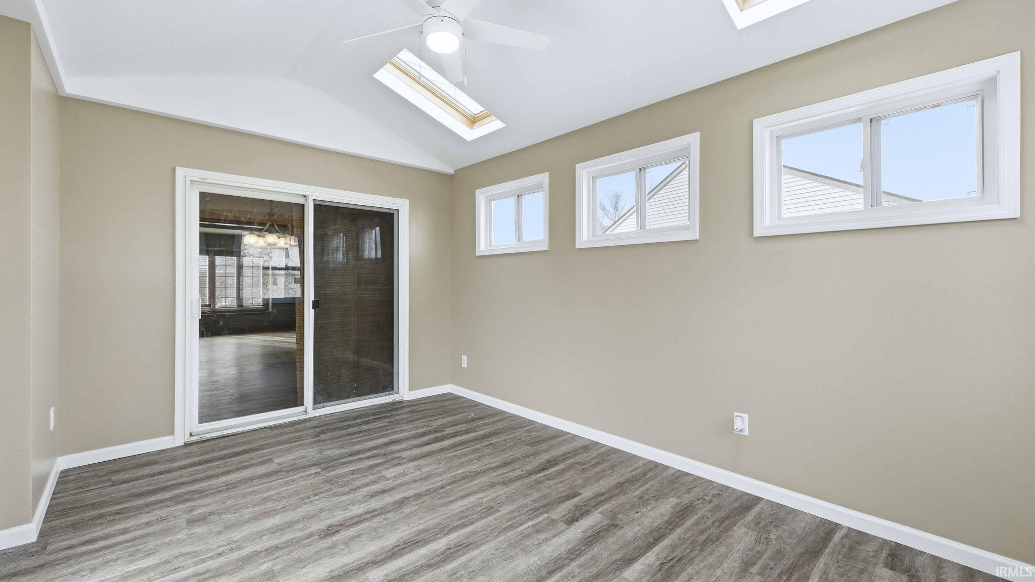 Unfurnished room featuring a skylight, vaulted ceiling, wood finished floors, and a ceiling fan