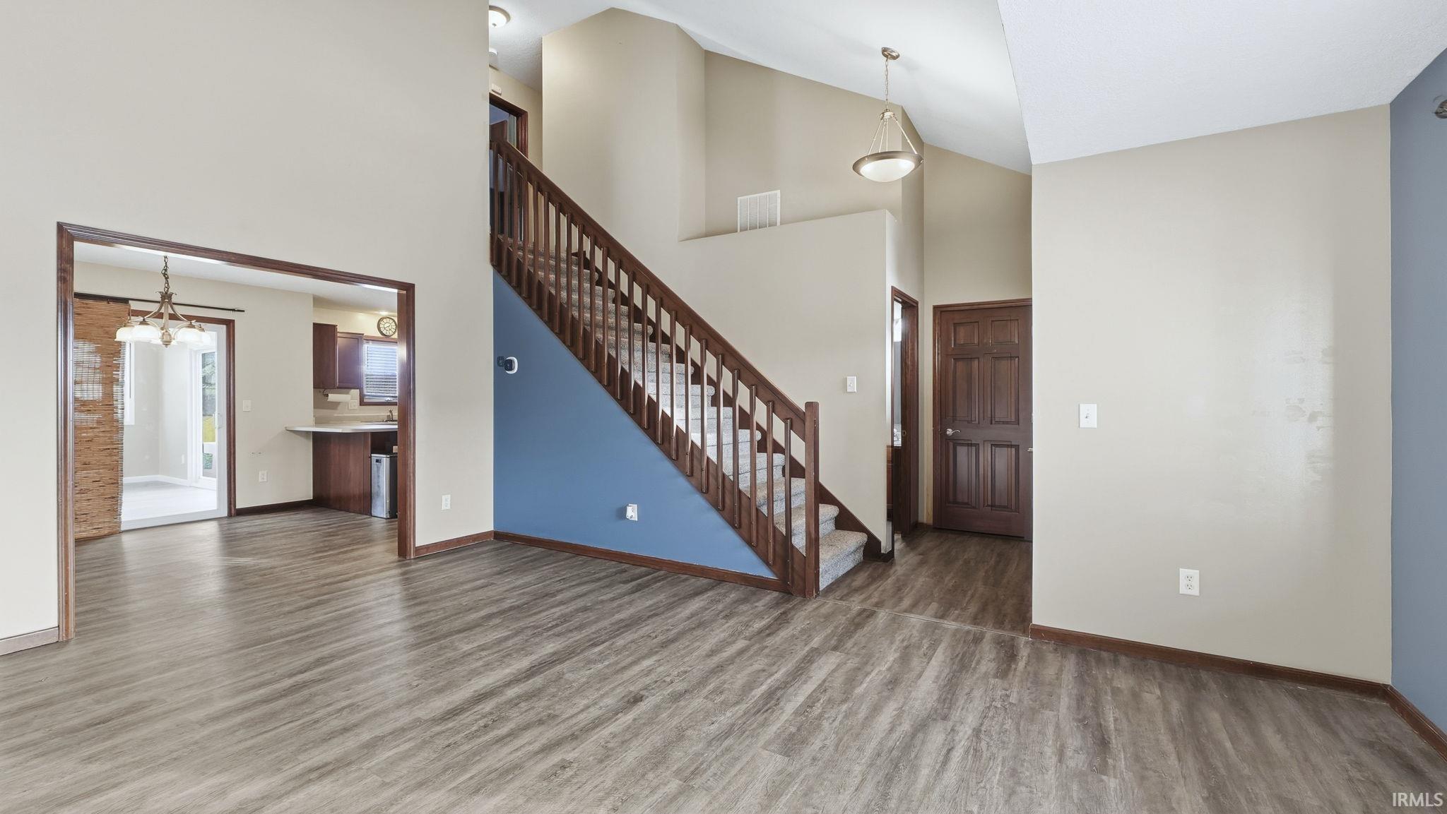 Unfurnished living room featuring high vaulted ceiling, stairway, a chandelier, and wood finished floors