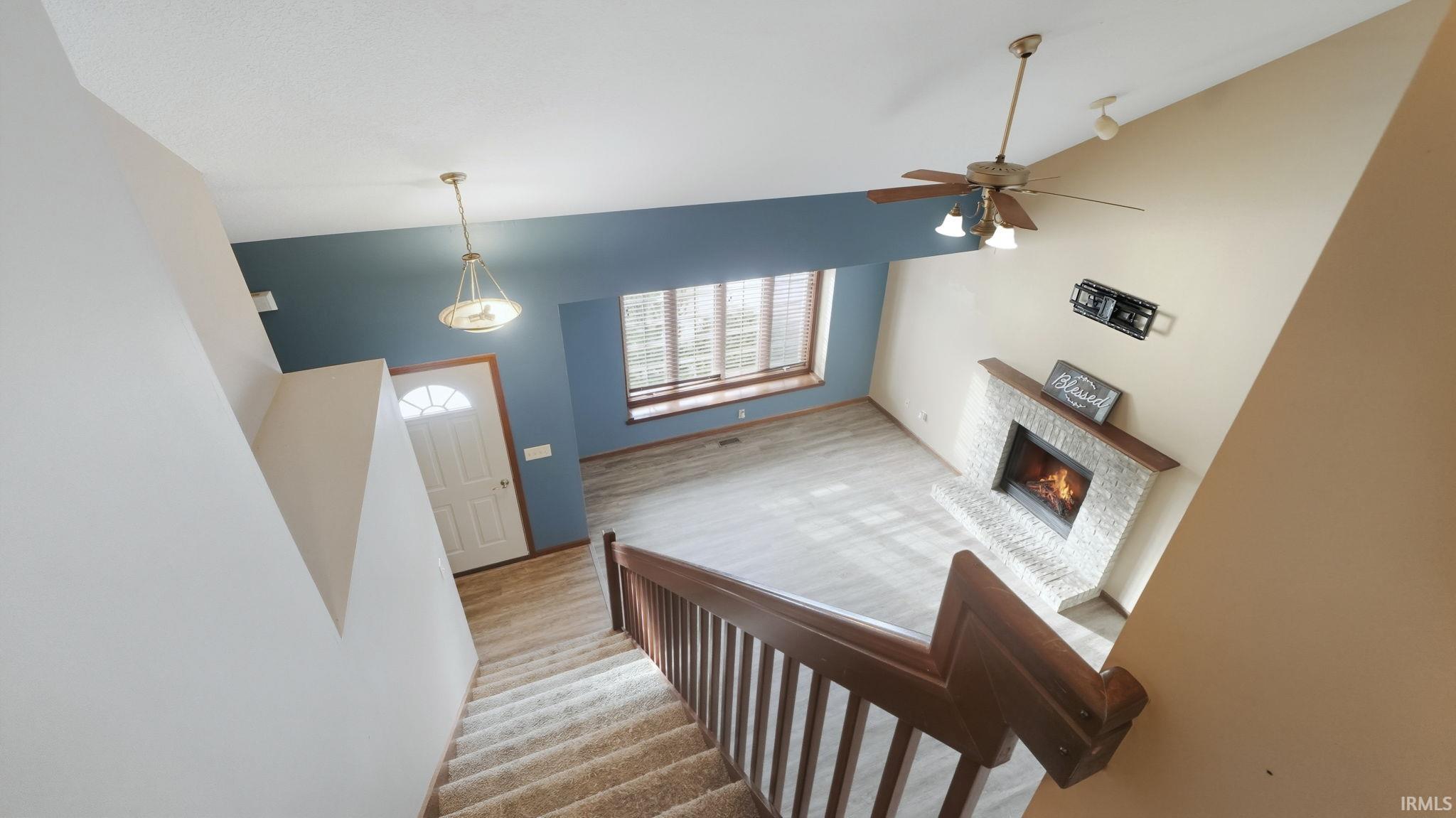 Stairway with a warm lit fireplace, a towering ceiling, wood finished floors, and a ceiling fan