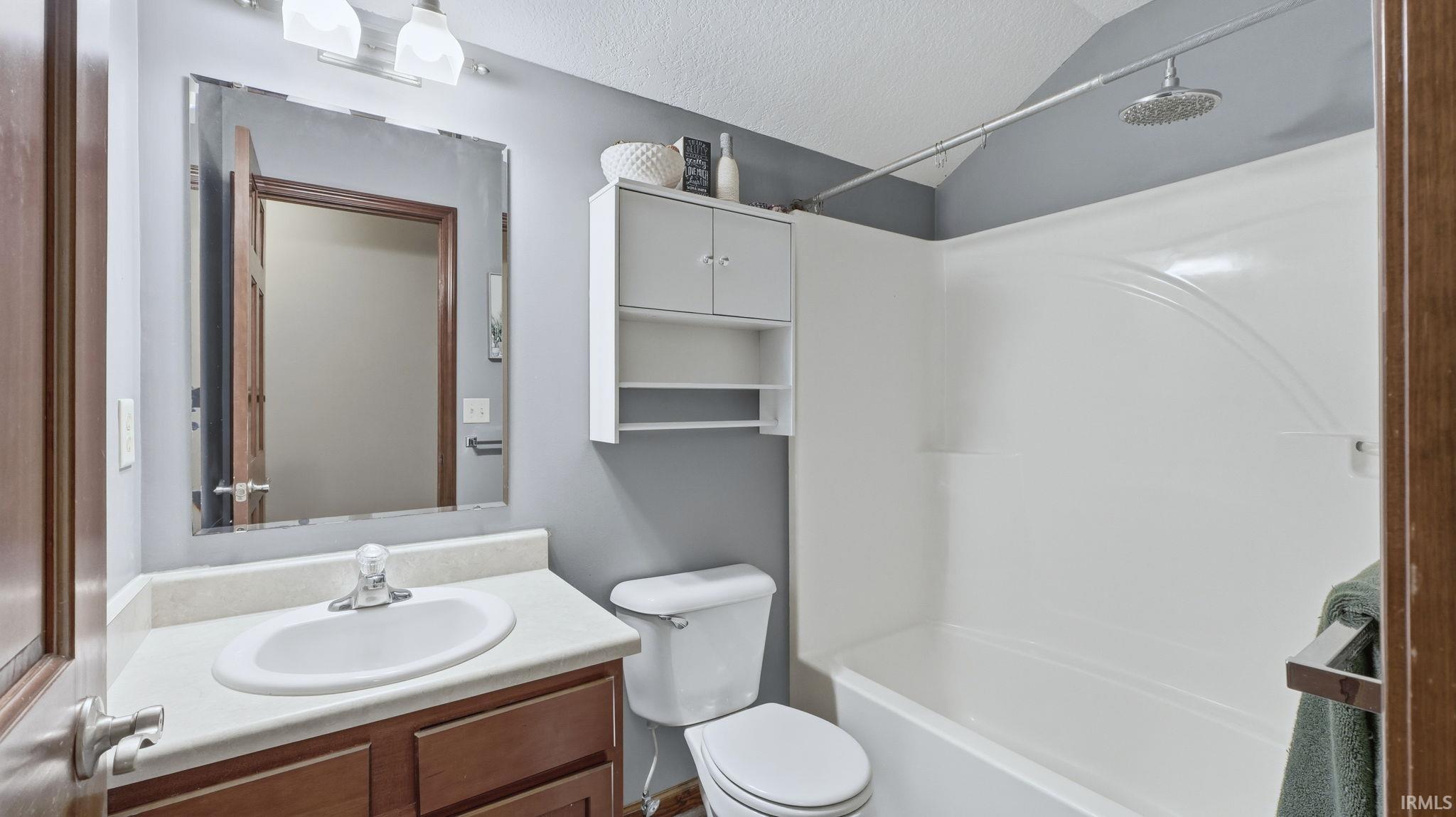 Full bath featuring lofted ceiling, vanity, a textured ceiling, and tub / shower combination
