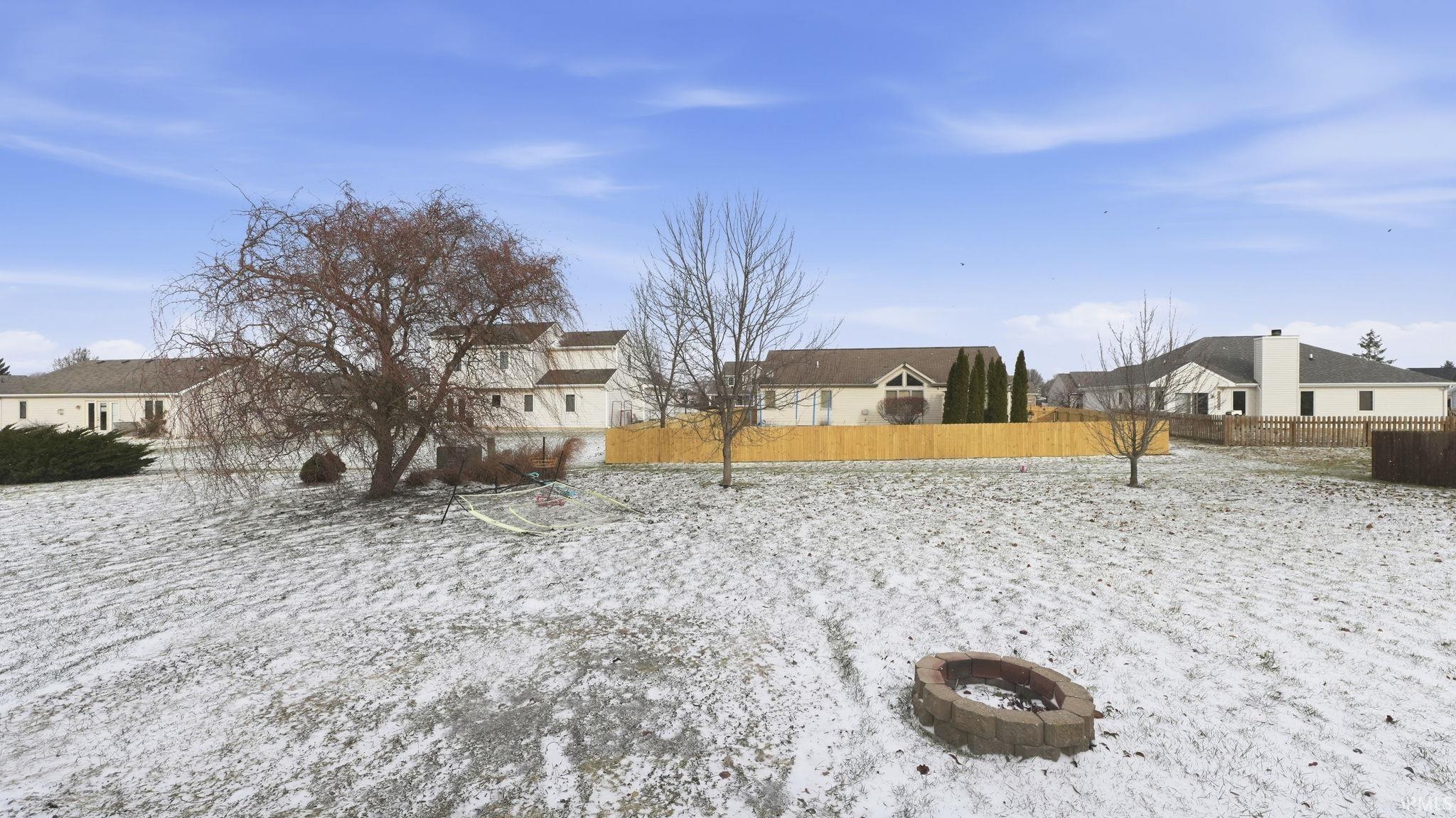 Yard covered in snow featuring an outdoor fire pit and a residential view