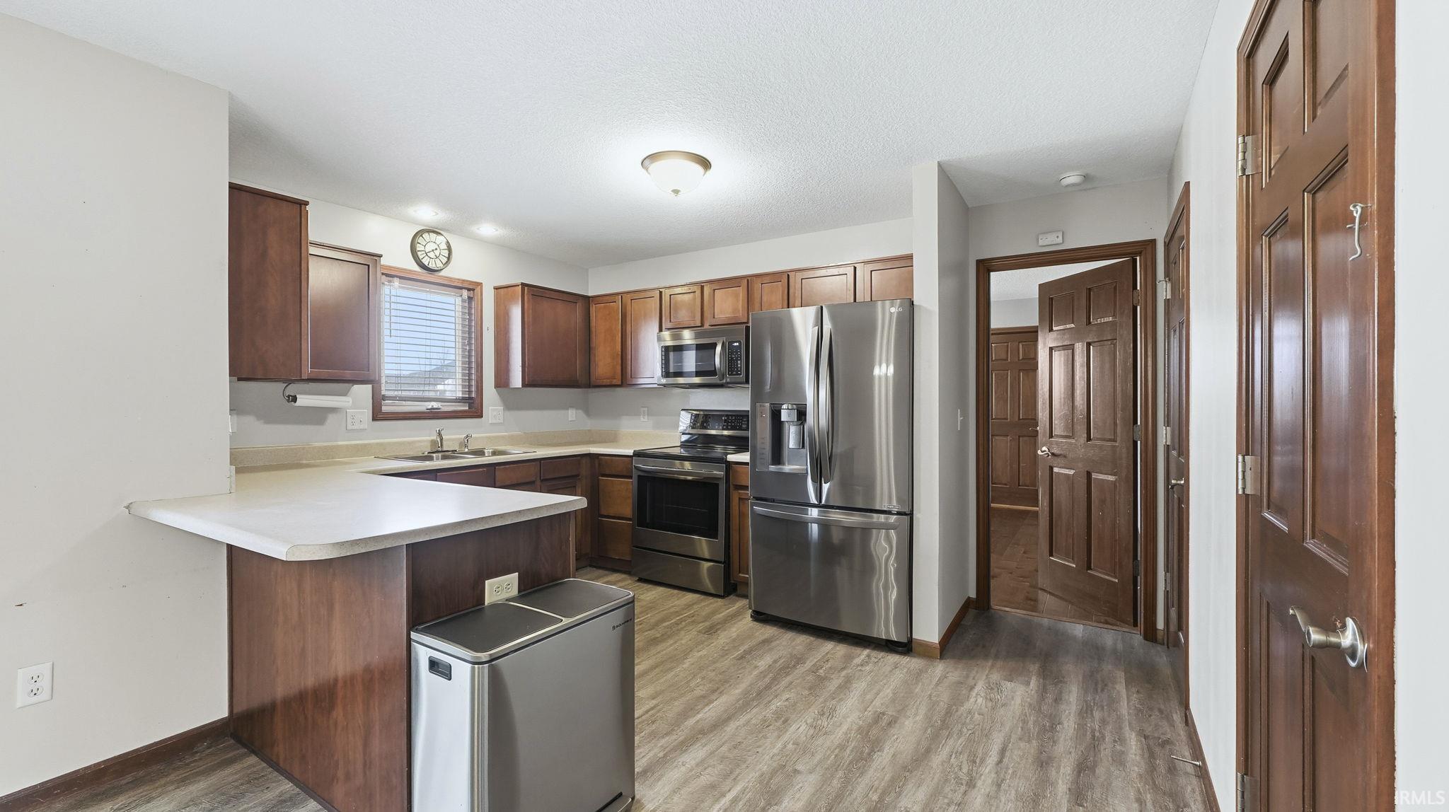 Kitchen featuring appliances with stainless steel finishes, light countertops, a peninsula, light wood-style floors, and a textured ceiling