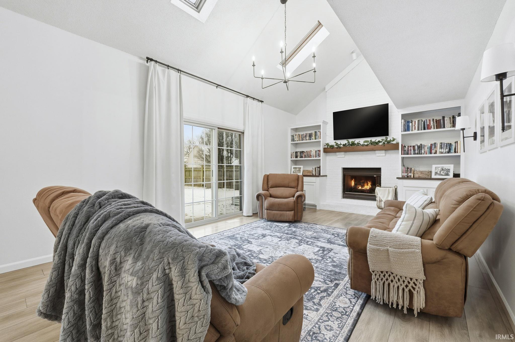Living area with a skylight, light wood-style flooring, a fireplace, built in shelves, and high vaulted ceiling