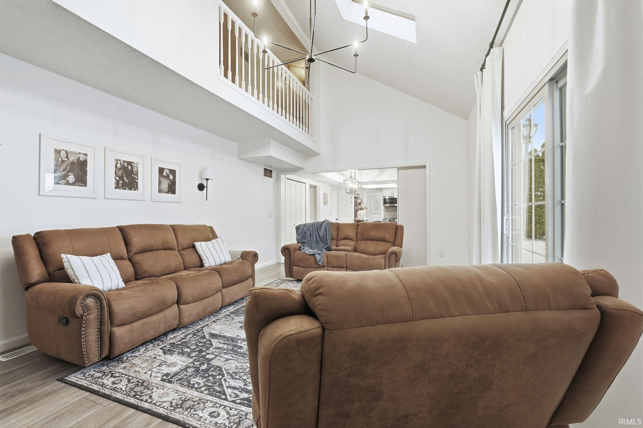 Living area featuring high vaulted ceiling, a chandelier, a skylight, and wood finished floors
