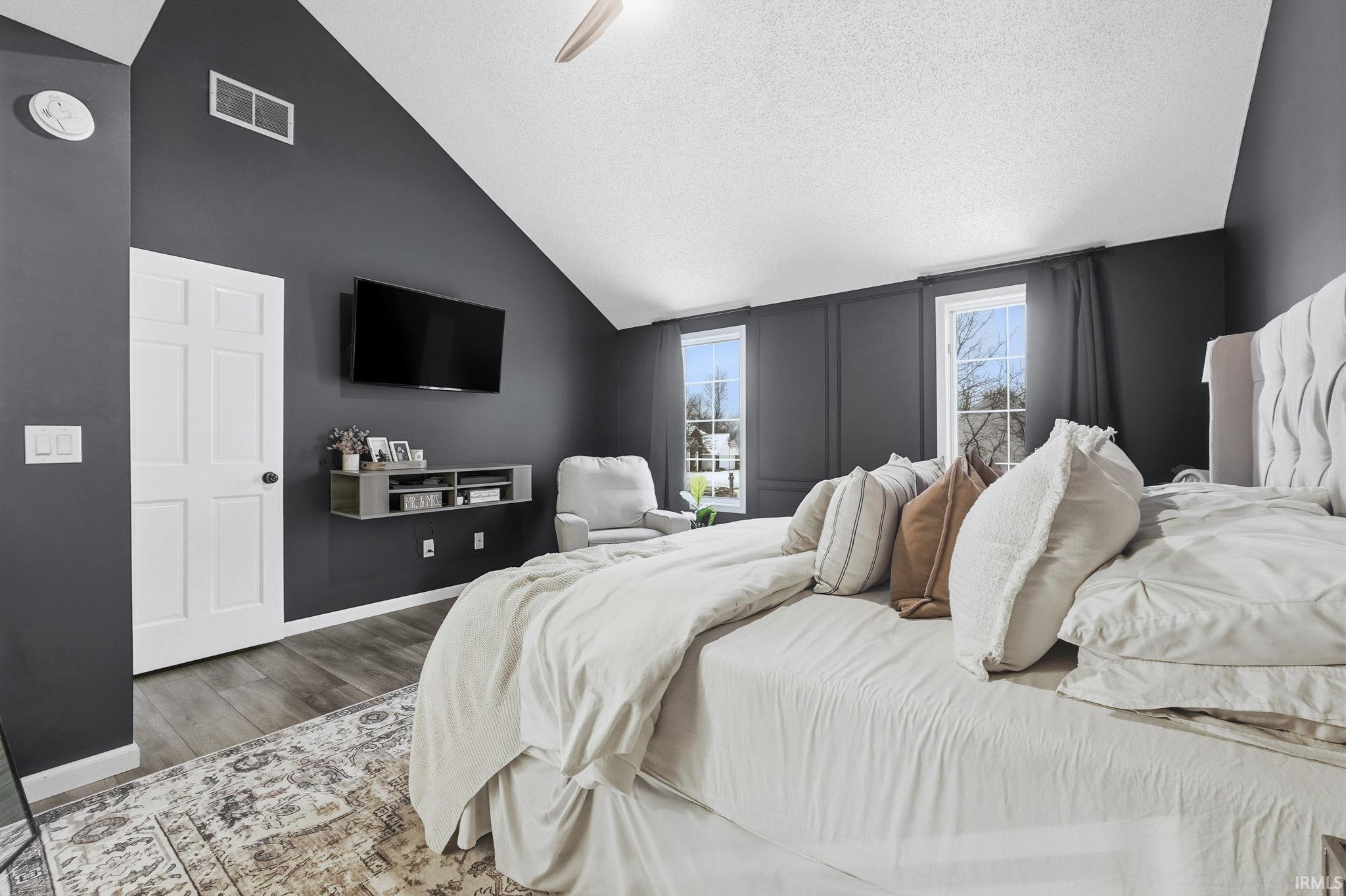 Bedroom with a textured ceiling, vaulted ceiling, ceiling fan, and wood finished floors