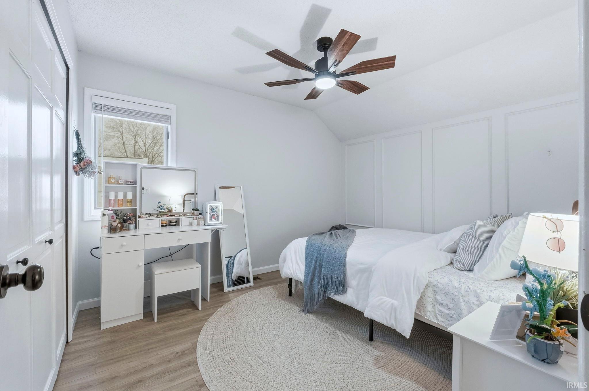 Bedroom featuring a decorative wall, light wood-style flooring, a ceiling fan, lofted ceiling, and a closet