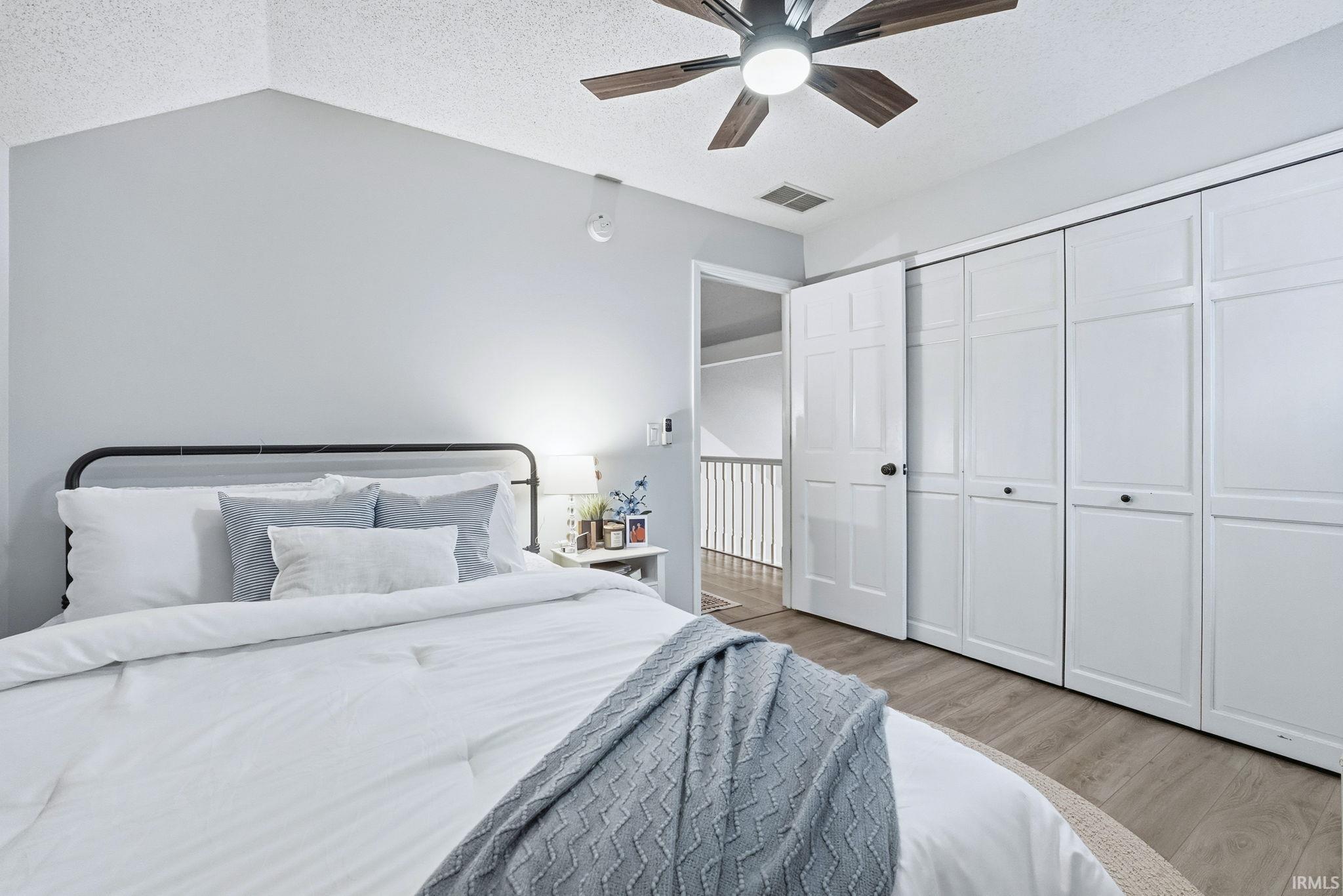 Bedroom with a textured ceiling, light wood-style floors, a ceiling fan, a closet, and lofted ceiling
