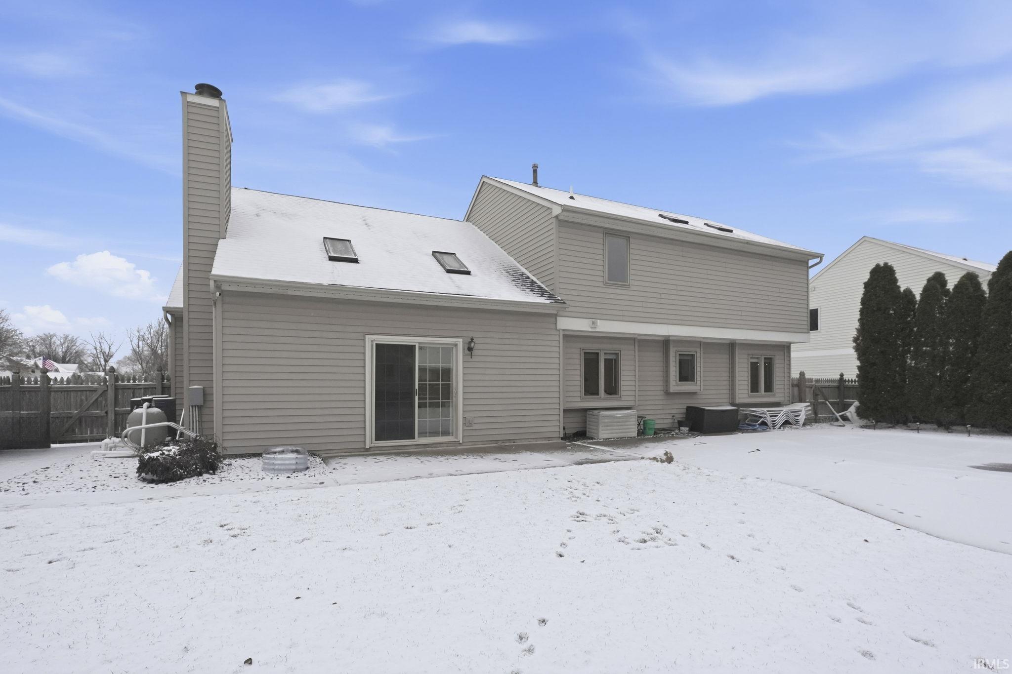 Snow covered back of property with a chimney and a patio