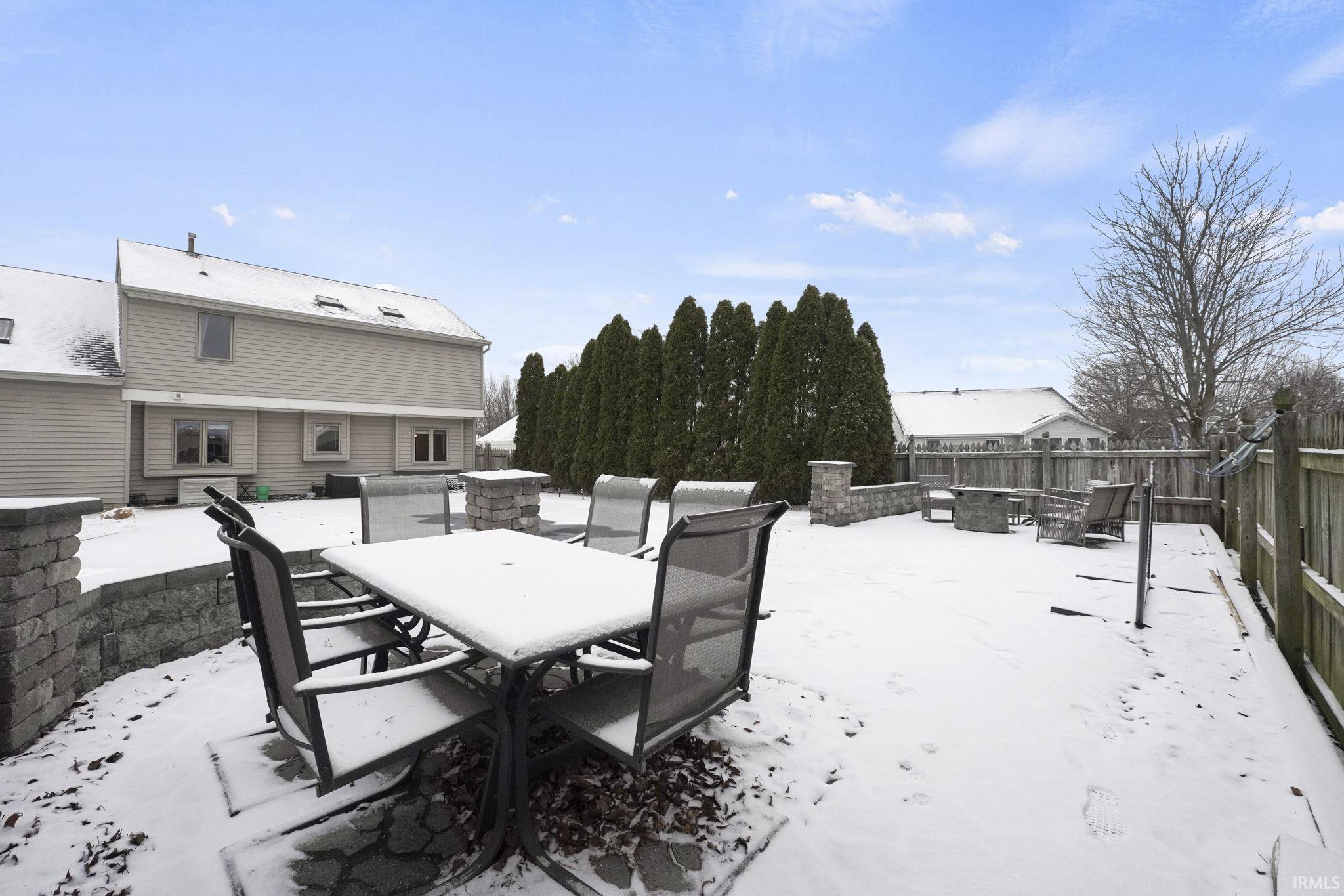 Snow covered patio with a fire pit, outdoor dining area, a wooden deck, and a fenced backyard
