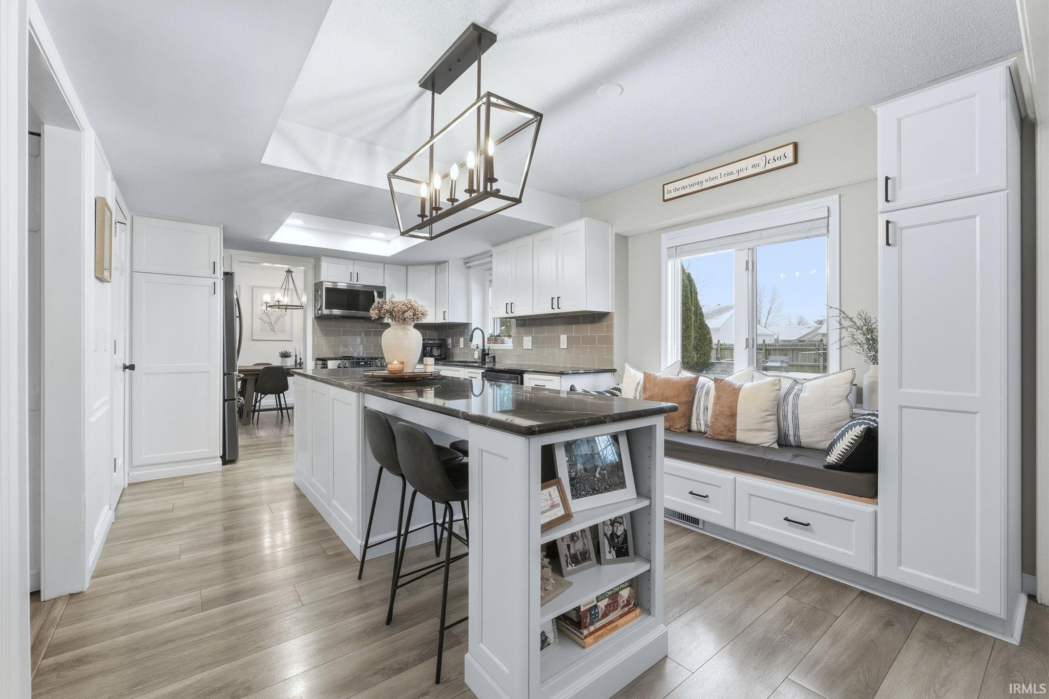 Kitchen with white cabinetry, decorative light fixtures, tasteful backsplash, a kitchen island, and light wood finished floors