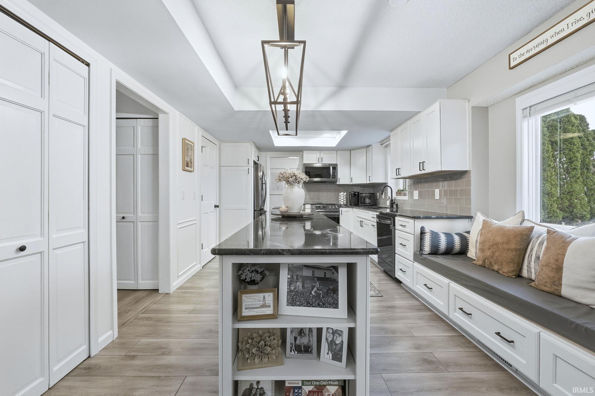 Kitchen featuring white cabinetry, a kitchen island, light wood-style flooring, dark stone countertops, and backsplash