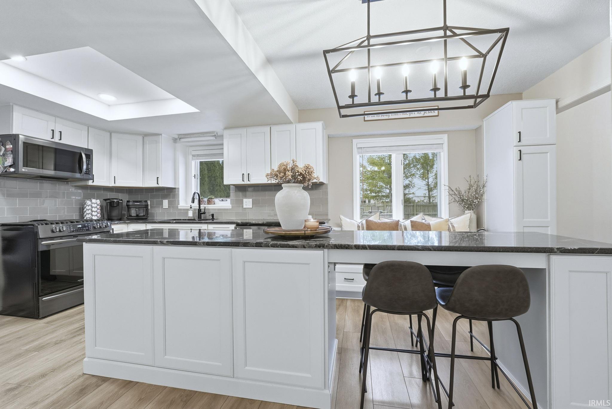 Kitchen with white cabinetry, appliances with stainless steel finishes, hanging light fixtures, backsplash, and dark stone counters